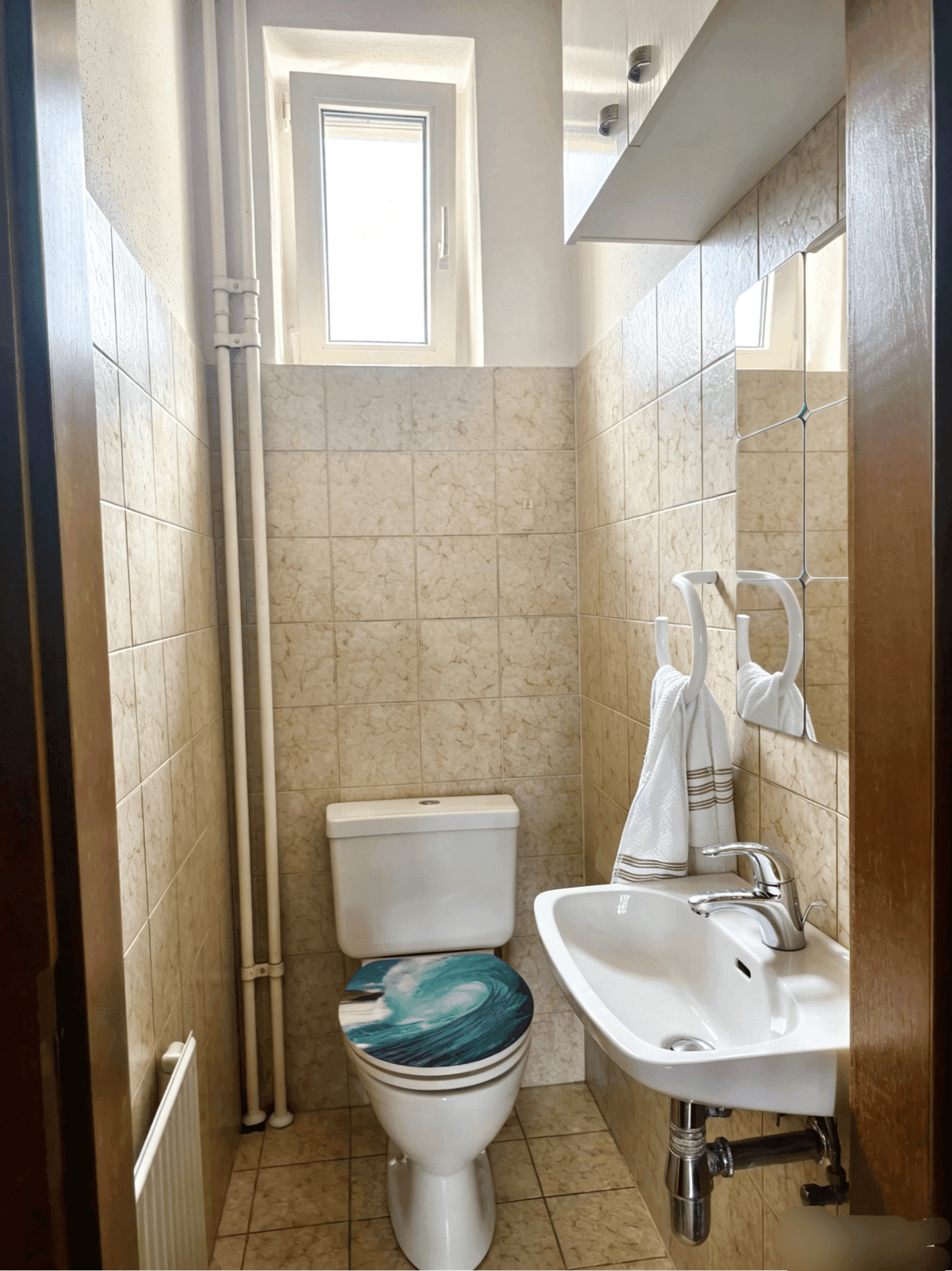 Kleines Gäste-WC mit beigefarbenen Fliesen, Fenster und einem modernen Waschbecken.