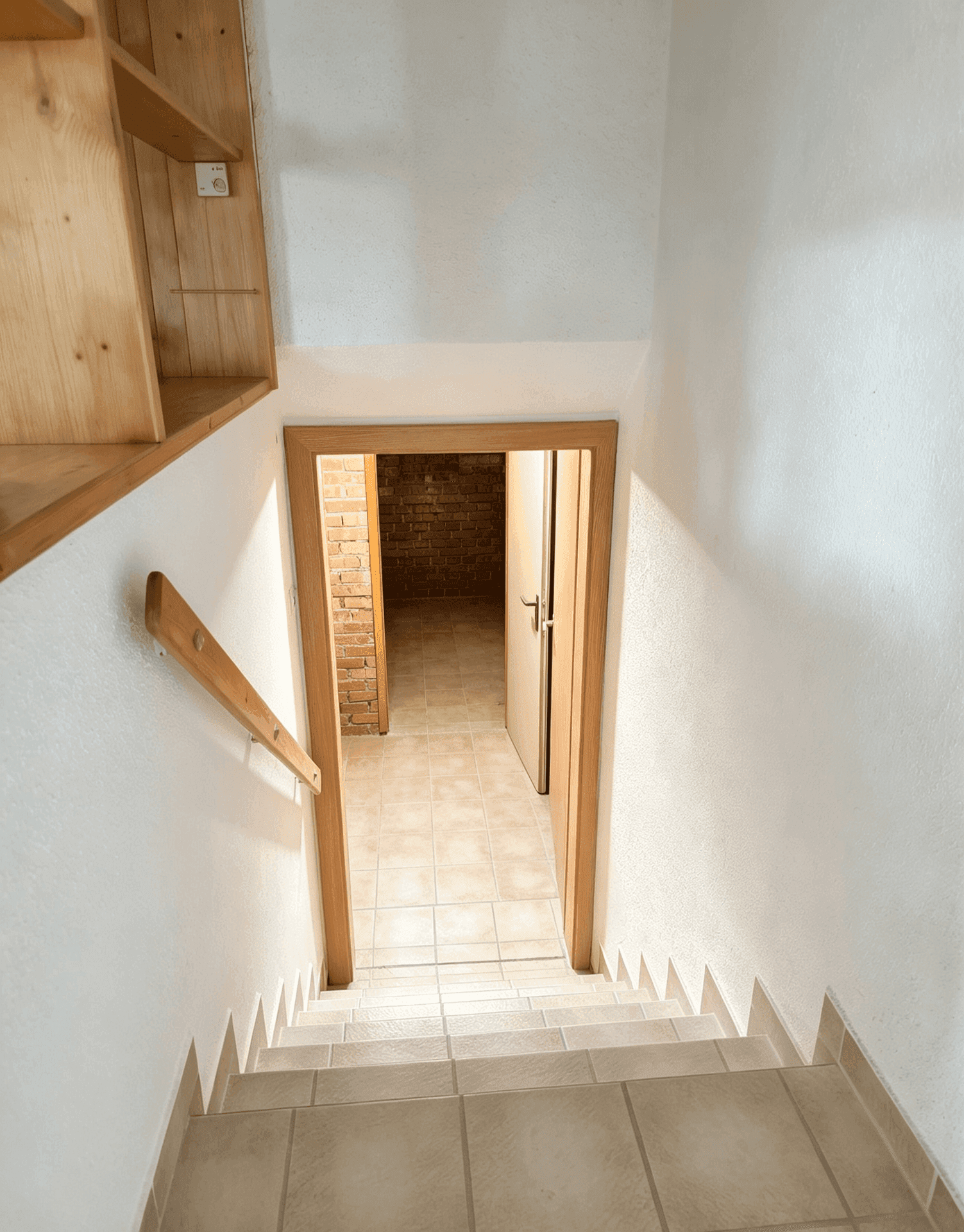 Treppe führt hinunter in den Kellerbereich mit Fliesenboden und Ziegelwänden.