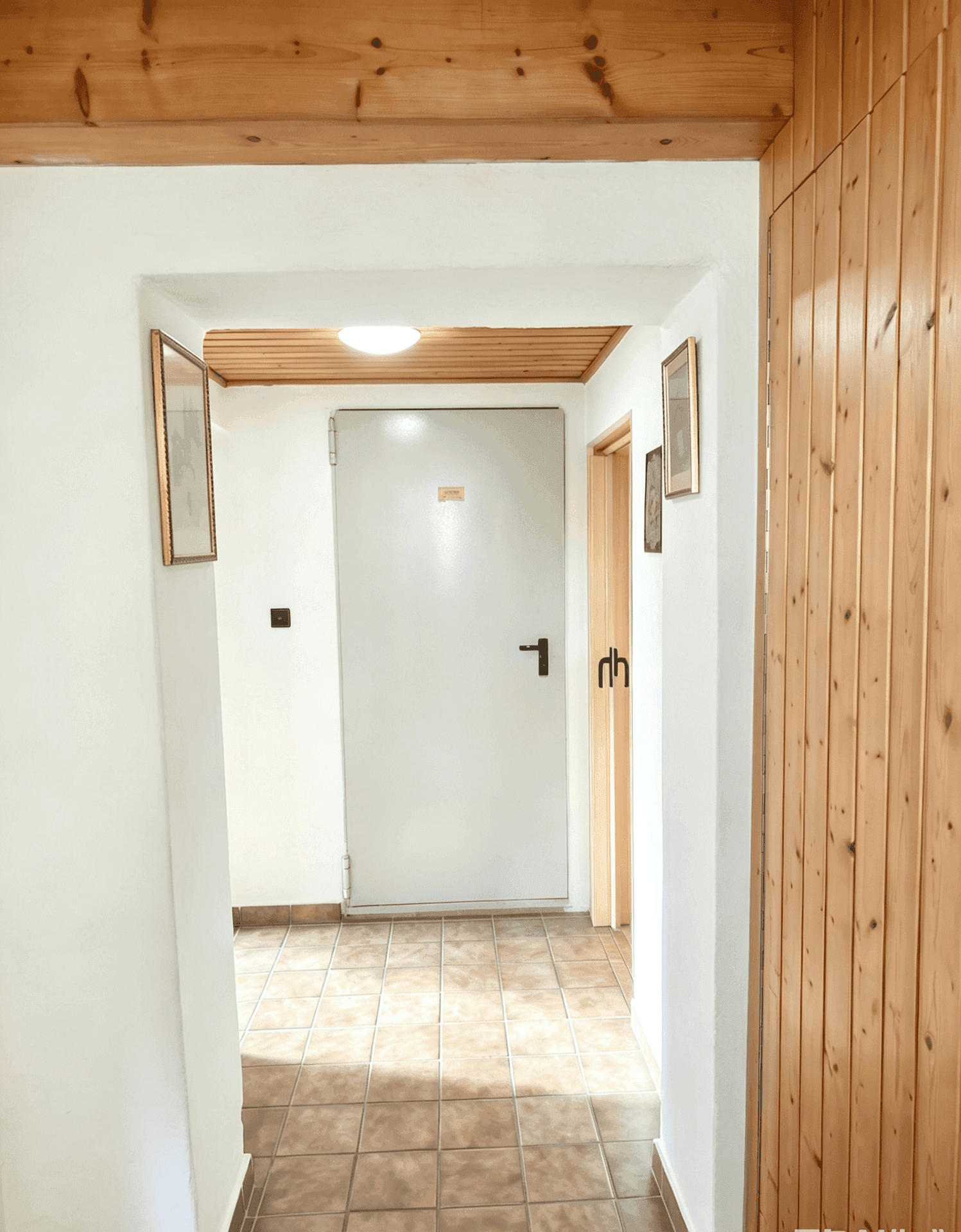 Heller Flur mit Fliesenboden, Holzdecke und einer weißen Eingangstür.