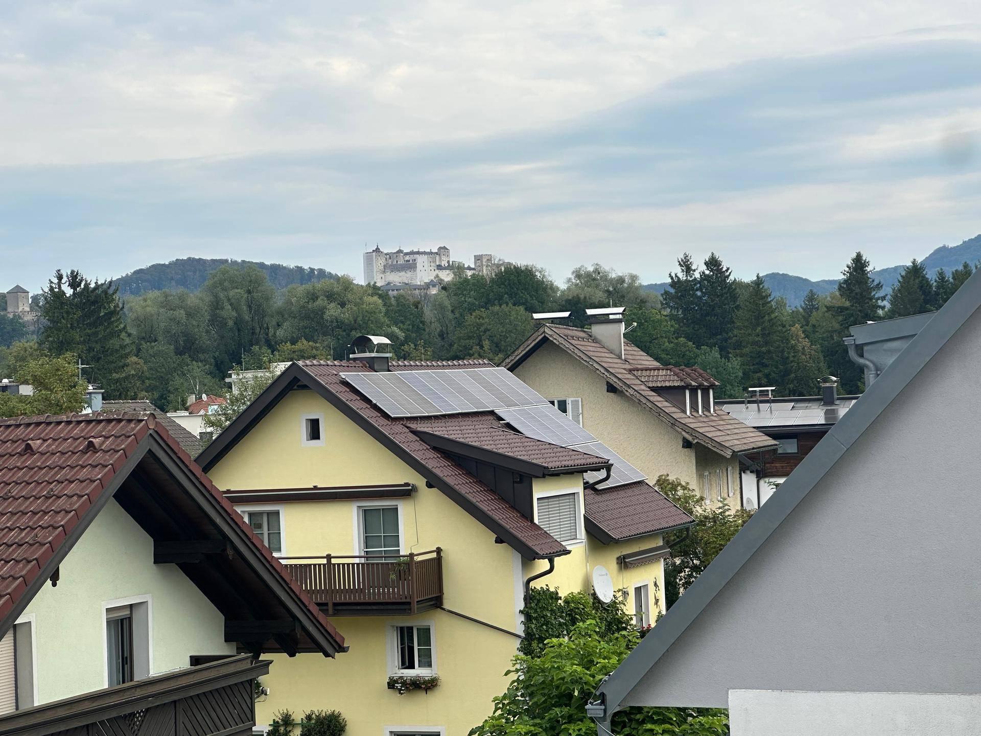 Blick über Dächer von Wohnhäusern mit Solaranlagen und einer Burg in der Ferne.