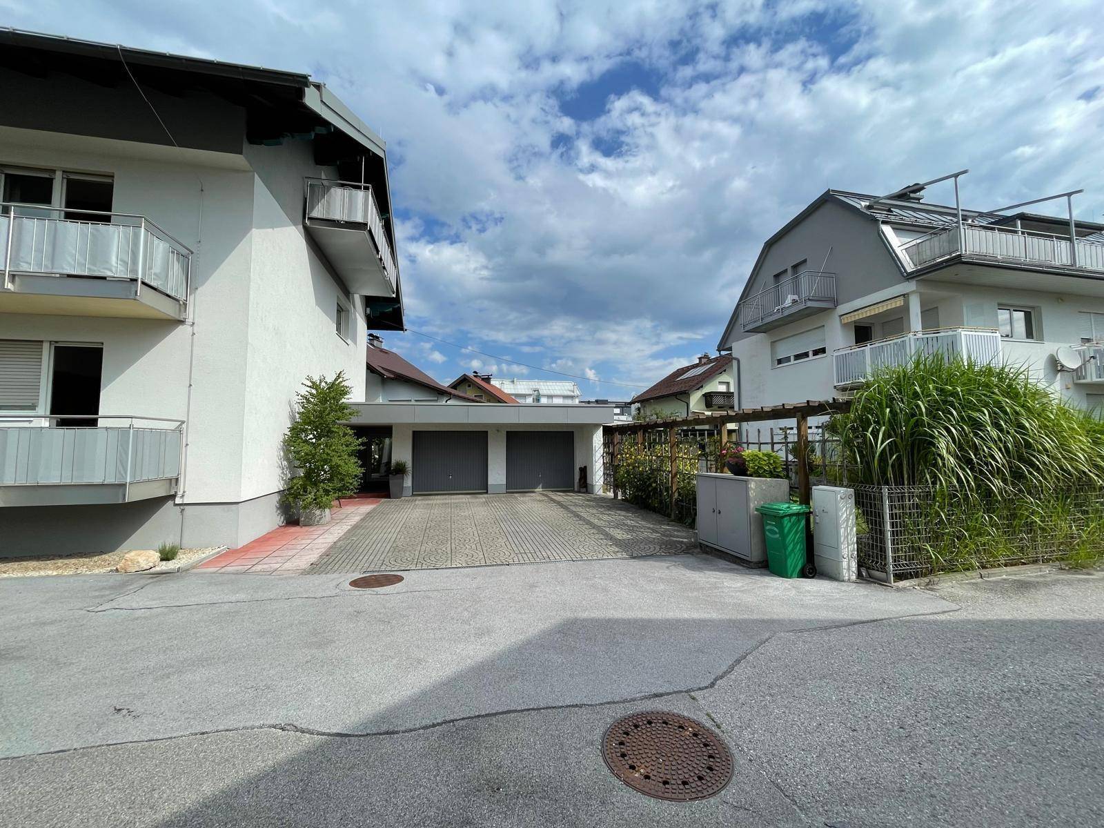 Einfahrt zu einer Doppelgarage zwischen zwei Wohngebäuden mit gepflastertem Vorplatz.