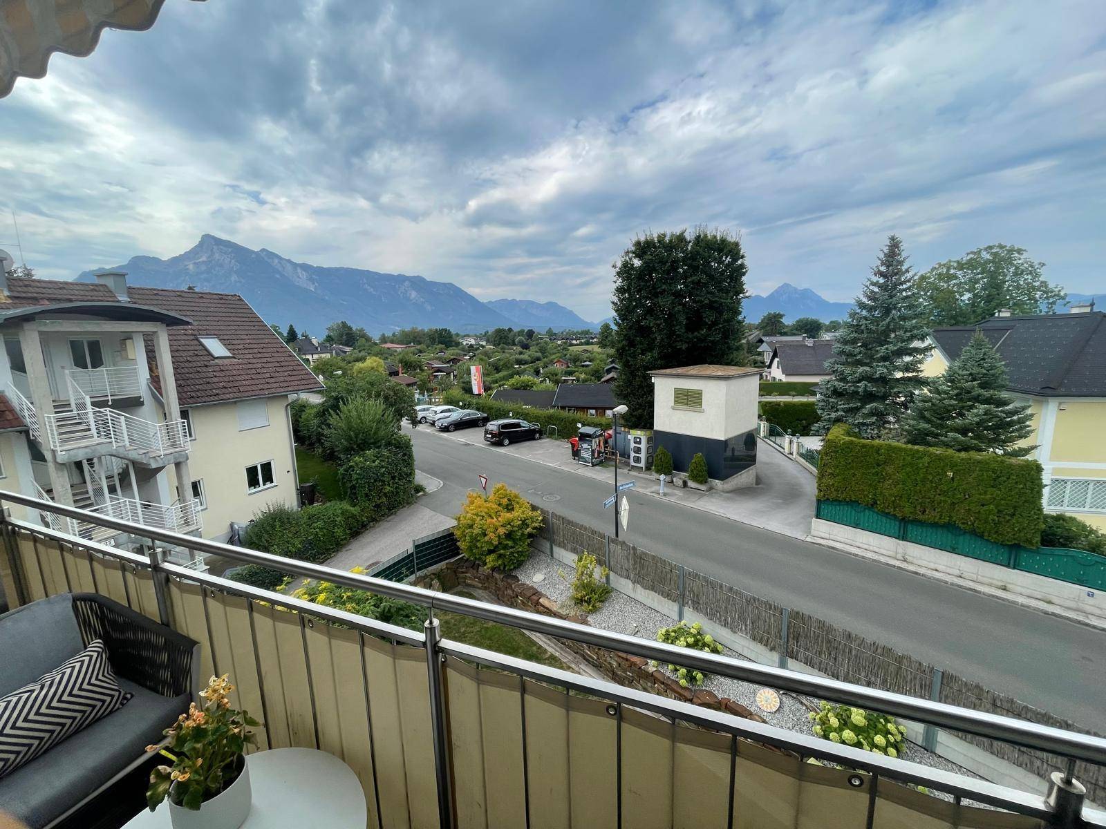 Blick vom Balkon mit Sitzgelegenheiten auf eine Straße und die umliegende Berglandschaft.