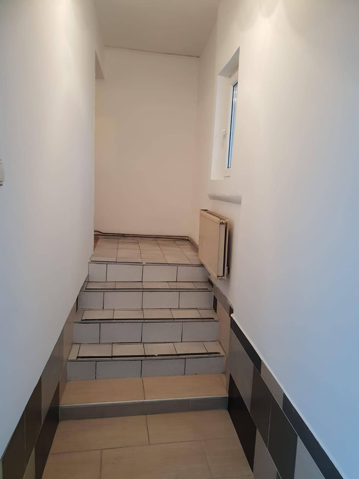 Treppenaufgang mit Fliesenstufen und einem Fenster, das Tageslicht hereinlässt.