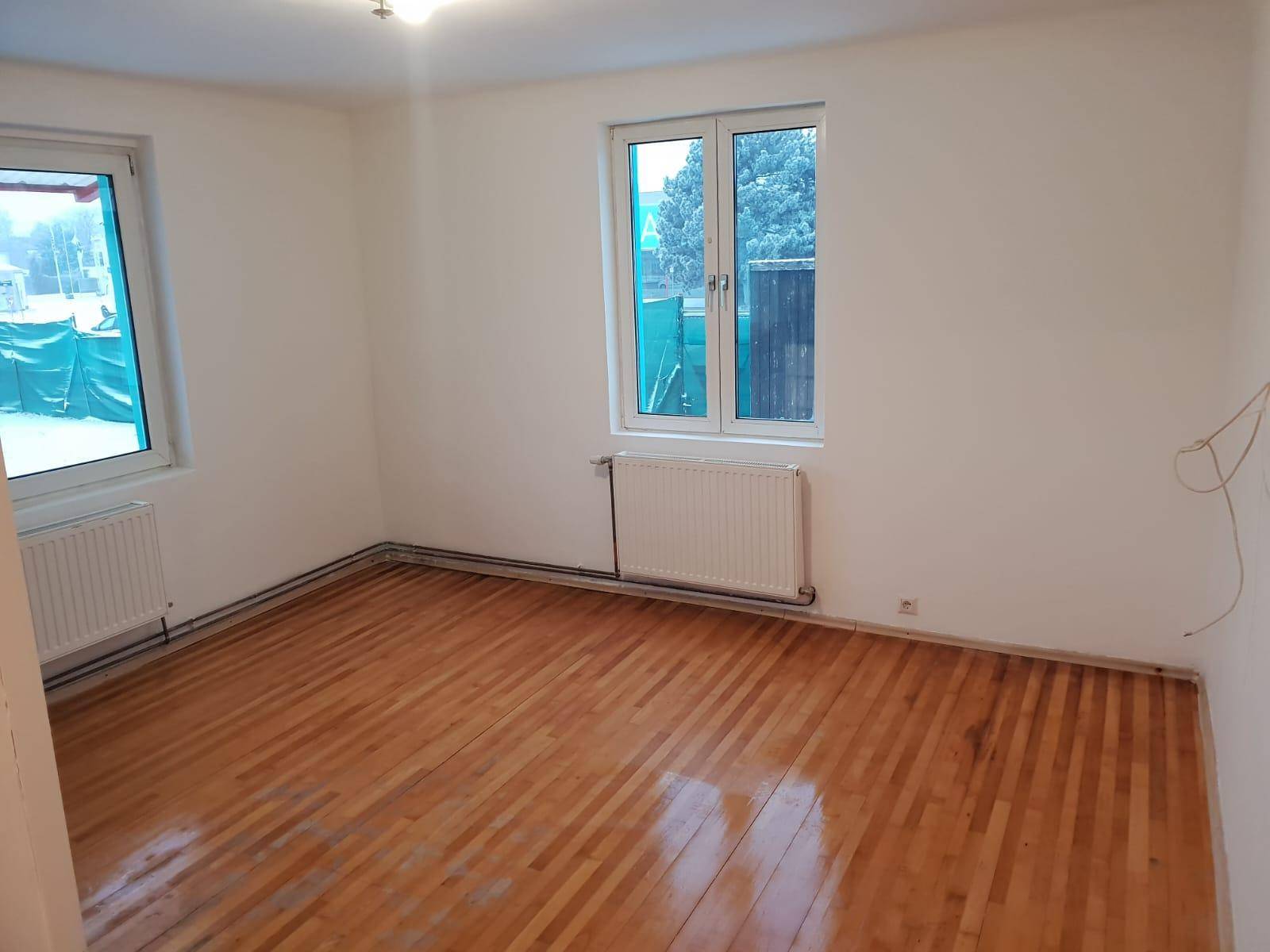 Heller Raum mit zwei Fenstern und Parkettboden, ideal für ein Schlafzimmer oder Büro.