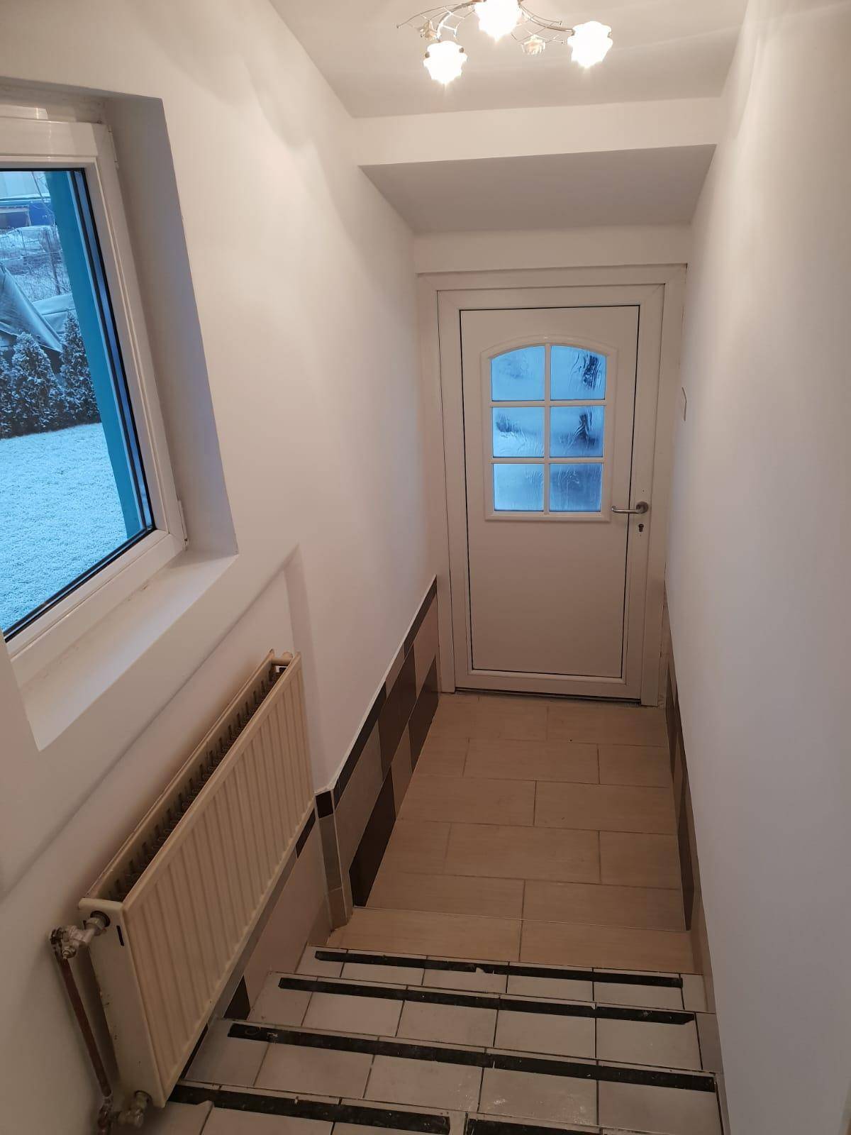 Eingangsbereich mit Treppe und einer hellen Tür mit Glaseinsätzen.