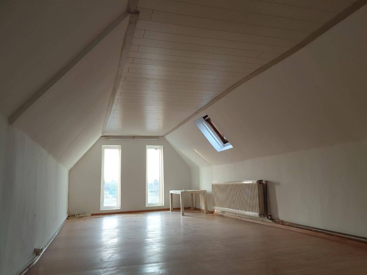 Heller Dachbodenraum mit schrägen Decken, zwei Fenstern und einem Dachfenster.