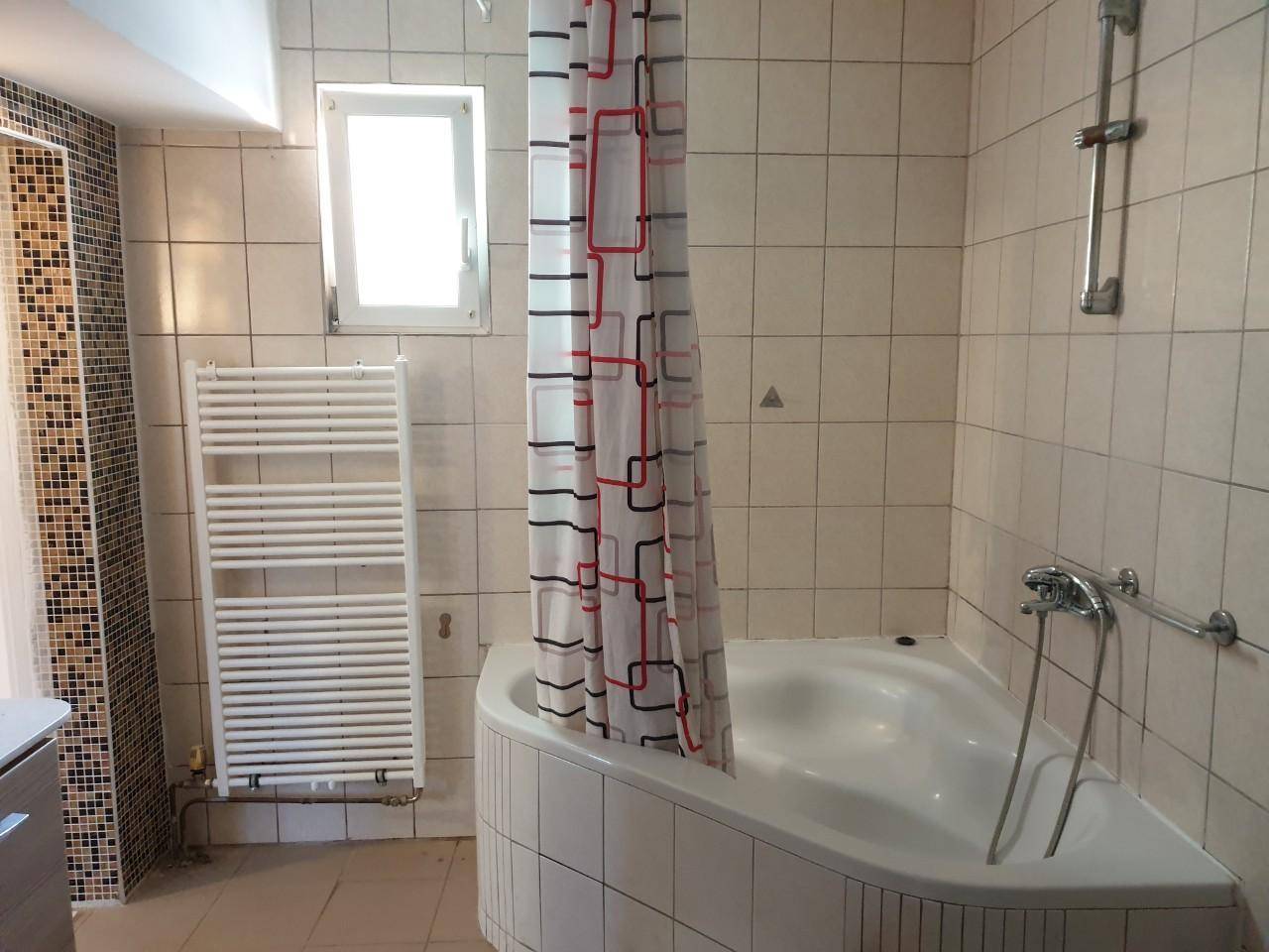 Badezimmer mit Eckbadewanne, Duschvorhang, beheiztem Handtuchhalter und Fenster.
