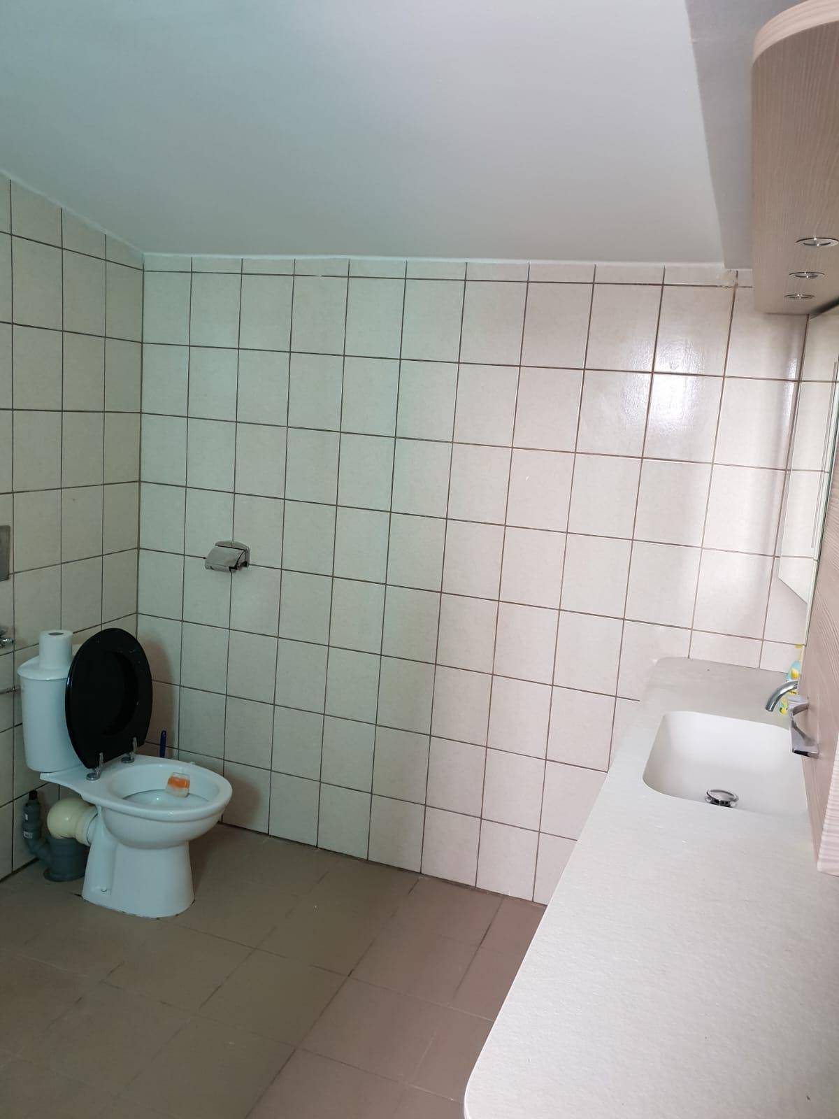 Badezimmer mit hellen Fliesen, Toilette und einem Waschbecken mit Unterschrank.