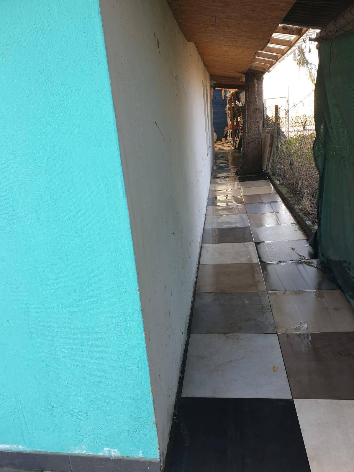 Gefliester Außenbereich entlang einer Gebäudewand mit türkisfarbenem Anstrich.