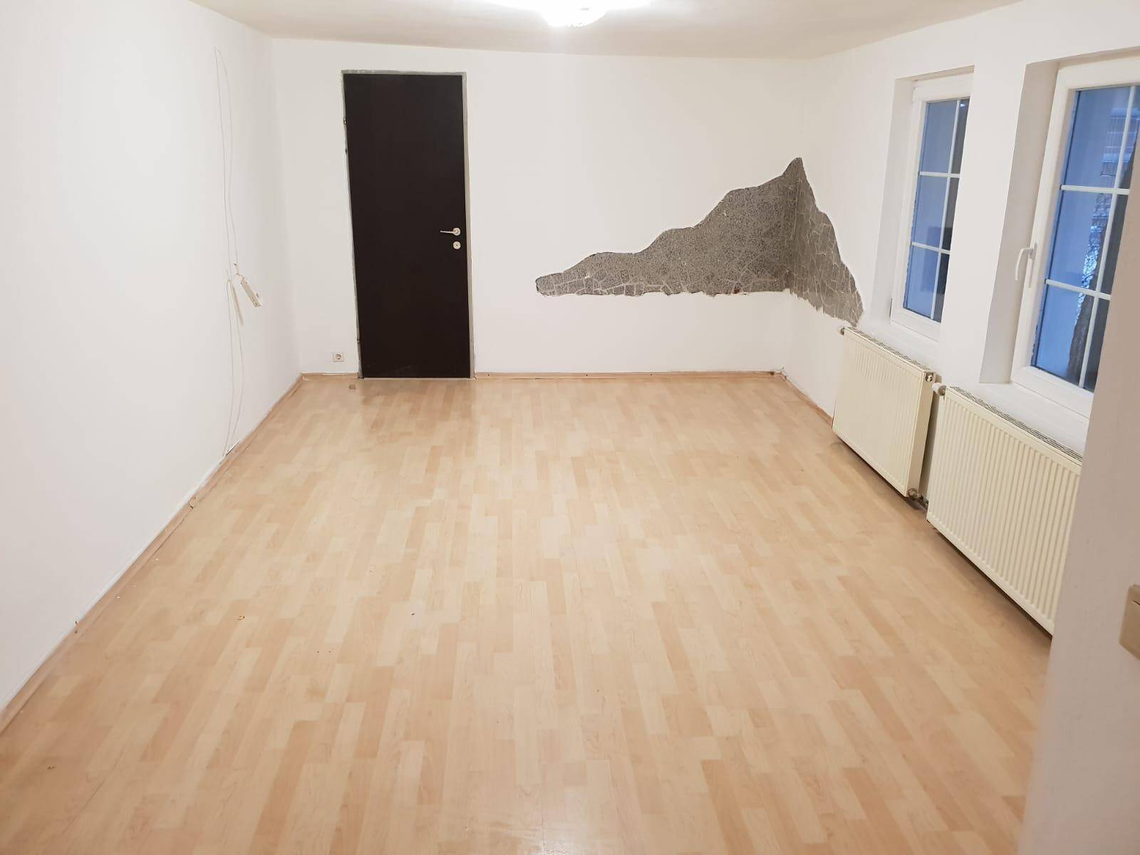 Geräumiger Raum mit Holzboden und einer dunklen Tür, bietet viel Gestaltungspotenzial.