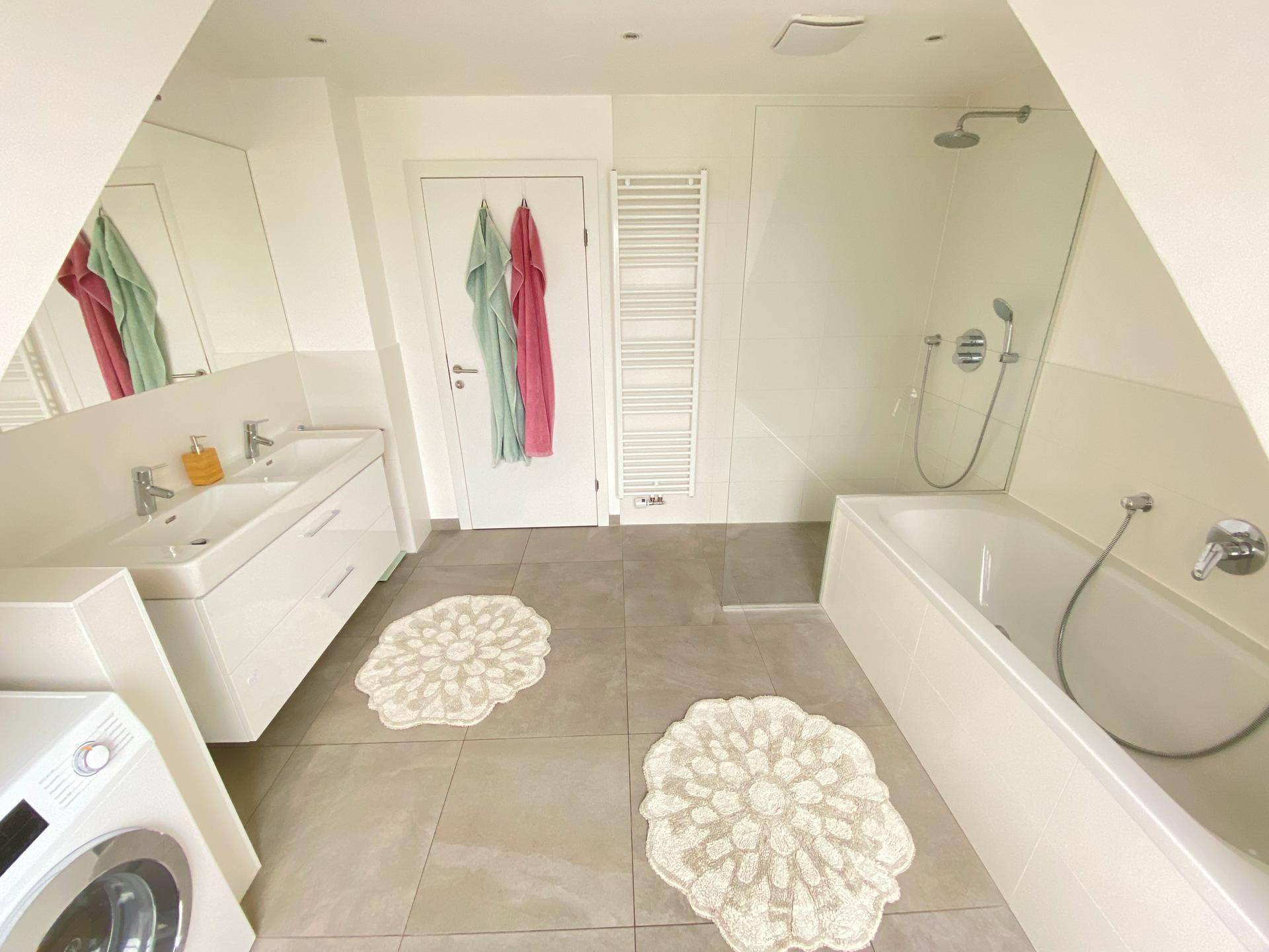 Modernes Badezimmer mit Doppelwaschbecken, Badewanne, Dusche und Fliesenboden.