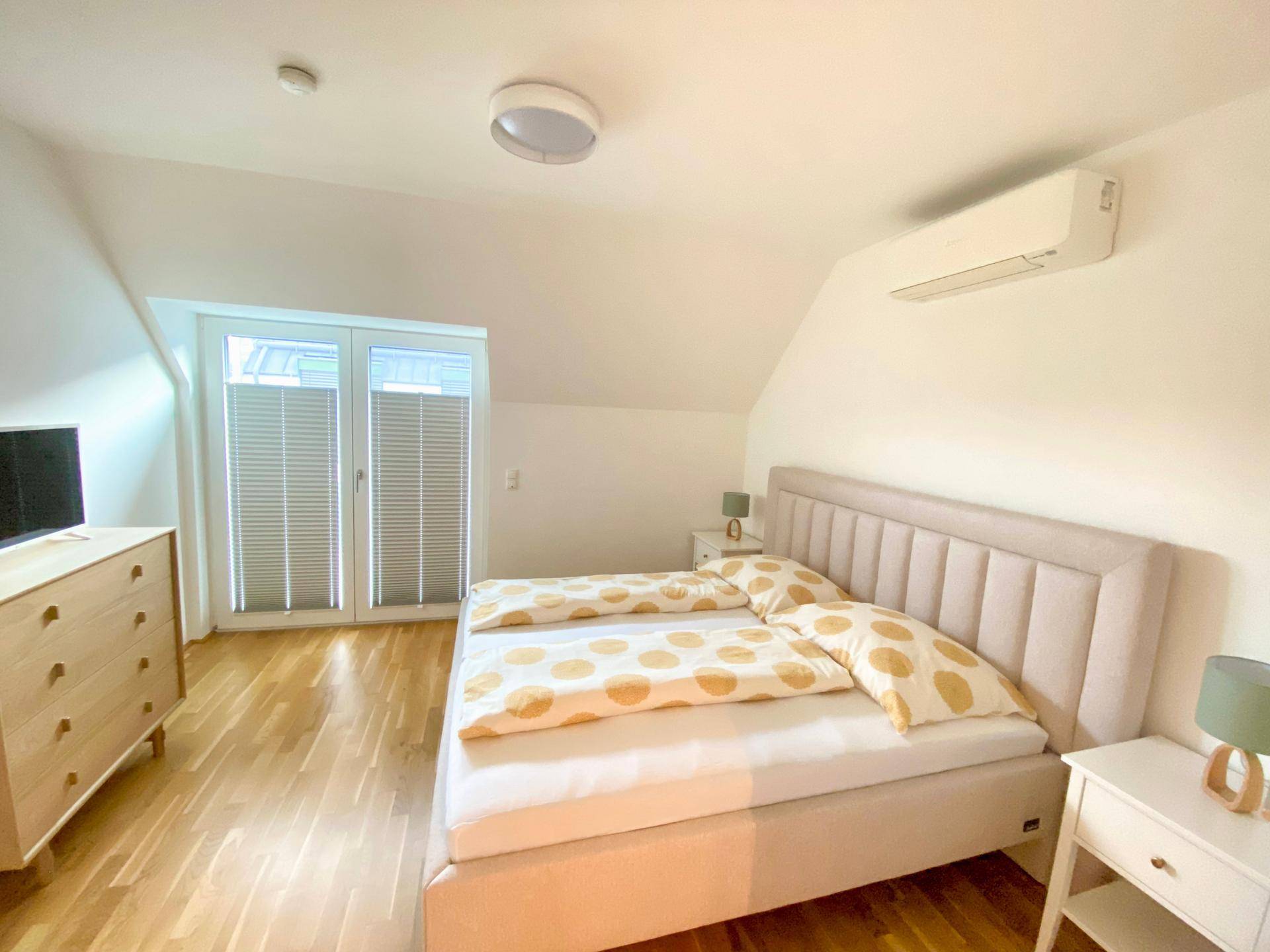 Helles Schlafzimmer mit Doppelbett, Holzboden, Dachschräge und Klimaanlage.