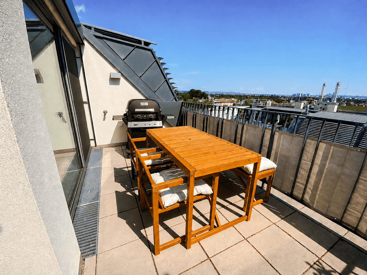 Sonnenterrasse mit Holztisch, Grill und weitem Blick über die Stadtlandschaft.