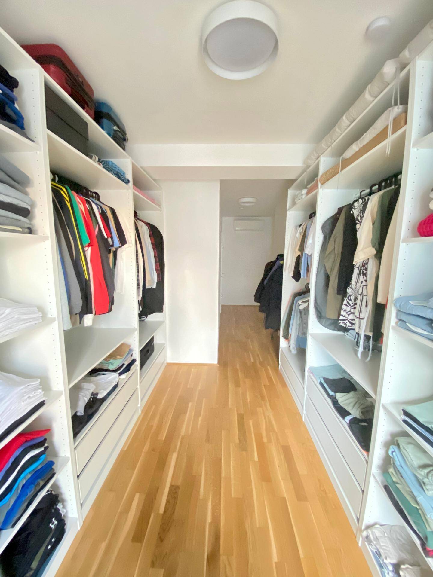 Geräumiger begehbarer Kleiderschrank mit viel Stauraum und Holzboden.
