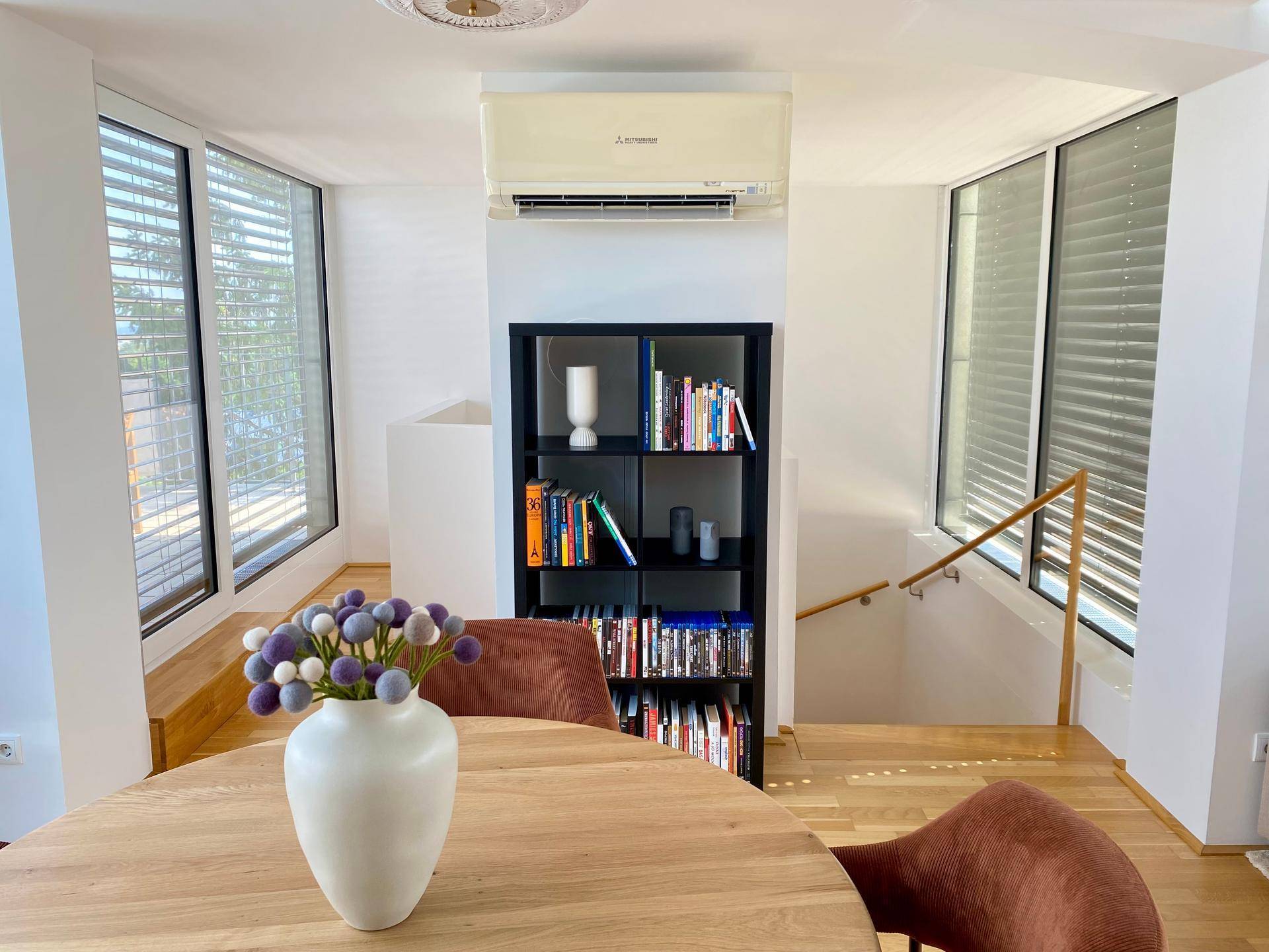 Heller Essbereich mit Holzboden, Bücherregal und Zugang zu einer Treppe.