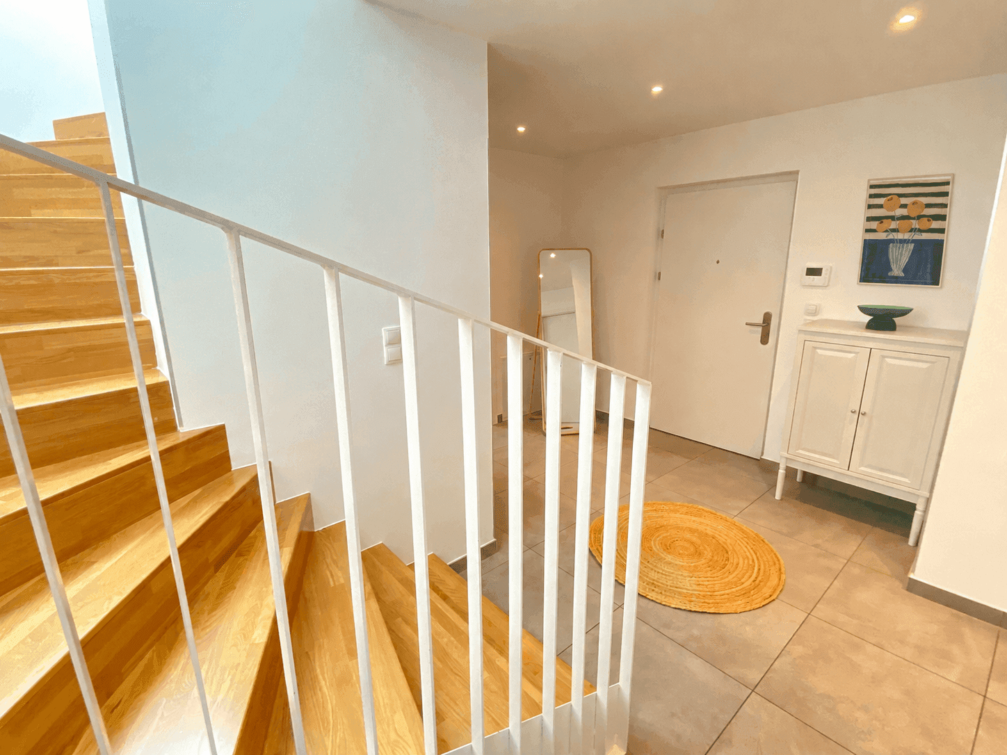 Heller Eingangsbereich mit Holztreppe, Fliesenboden und moderner Einrichtung.
