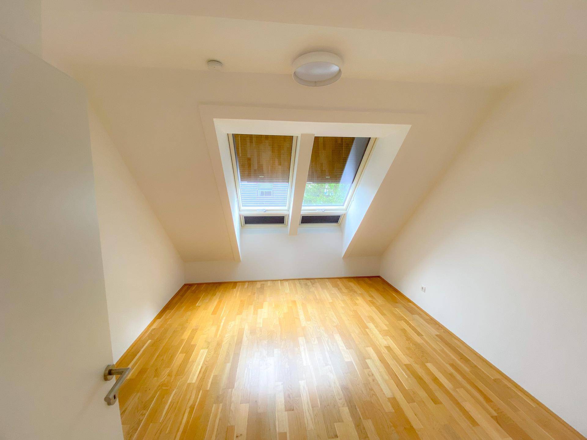 Helles Zimmer mit Holzboden, Dachschräge und Dachfenstern, ideal als Schlafzimmer.