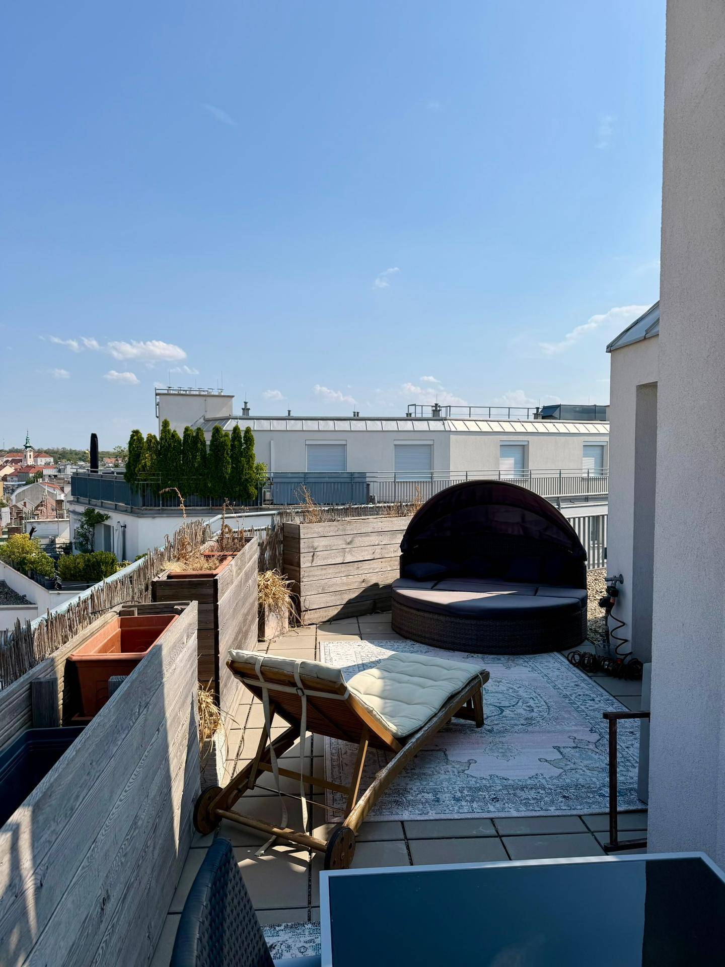 Geräumige Dachterrasse mit luxuriösem Tagesbett, Liegestuhl und weitem Stadtblick.
