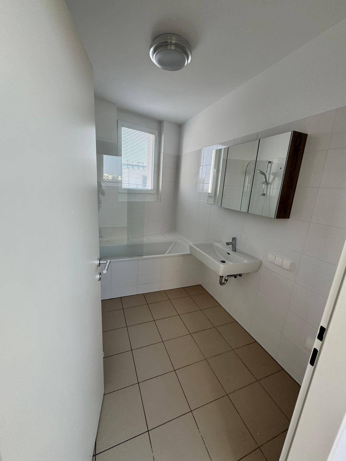Modernes Badezimmer mit Badewanne, Waschbecken, Spiegelschrank und Fliesenboden.