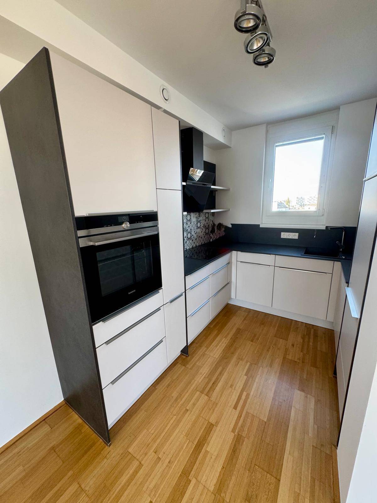 Moderne Küche mit weißen und dunkelgrauen Schränken, integriertem Backofen und Fenster.