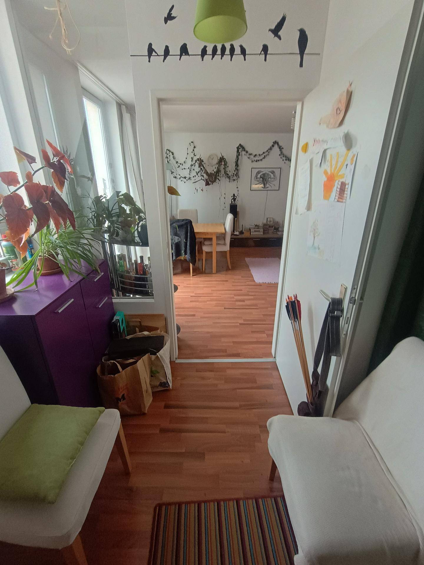 Flur mit Holzboden und Blick in den hellen Wohnbereich, dekoriert mit Pflanzen und Kunst.