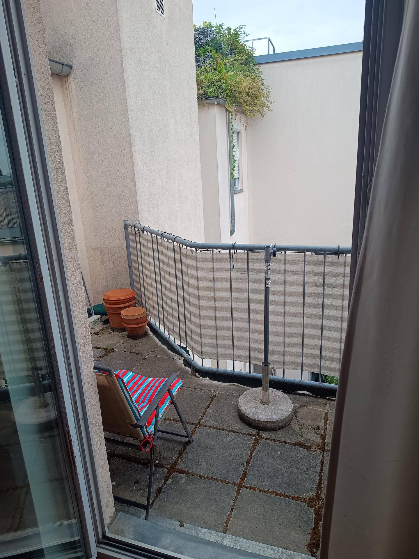 Gemütlicher Balkon mit Sitzgelegenheit und Topfpflanzen, umgeben von Gebäuden.