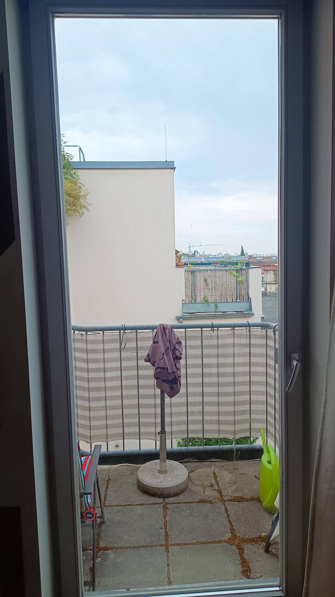 Blick vom Innenraum auf den Balkon mit Stadtansicht und umliegenden Gebäuden.