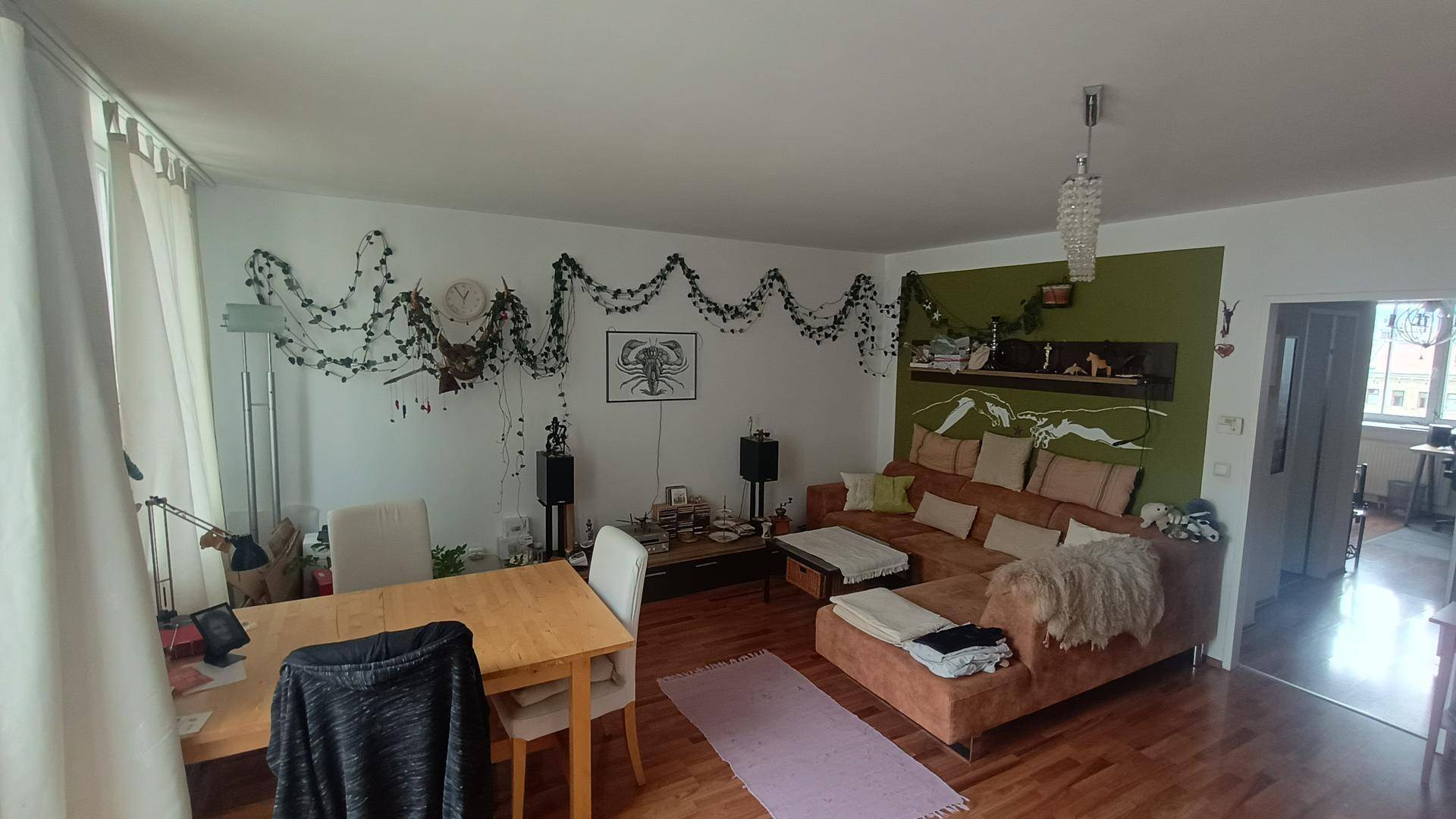 Helles Wohnzimmer mit Essbereich, Holzboden und gemütlicher Sitzecke, dekoriert mit Pflanzen.