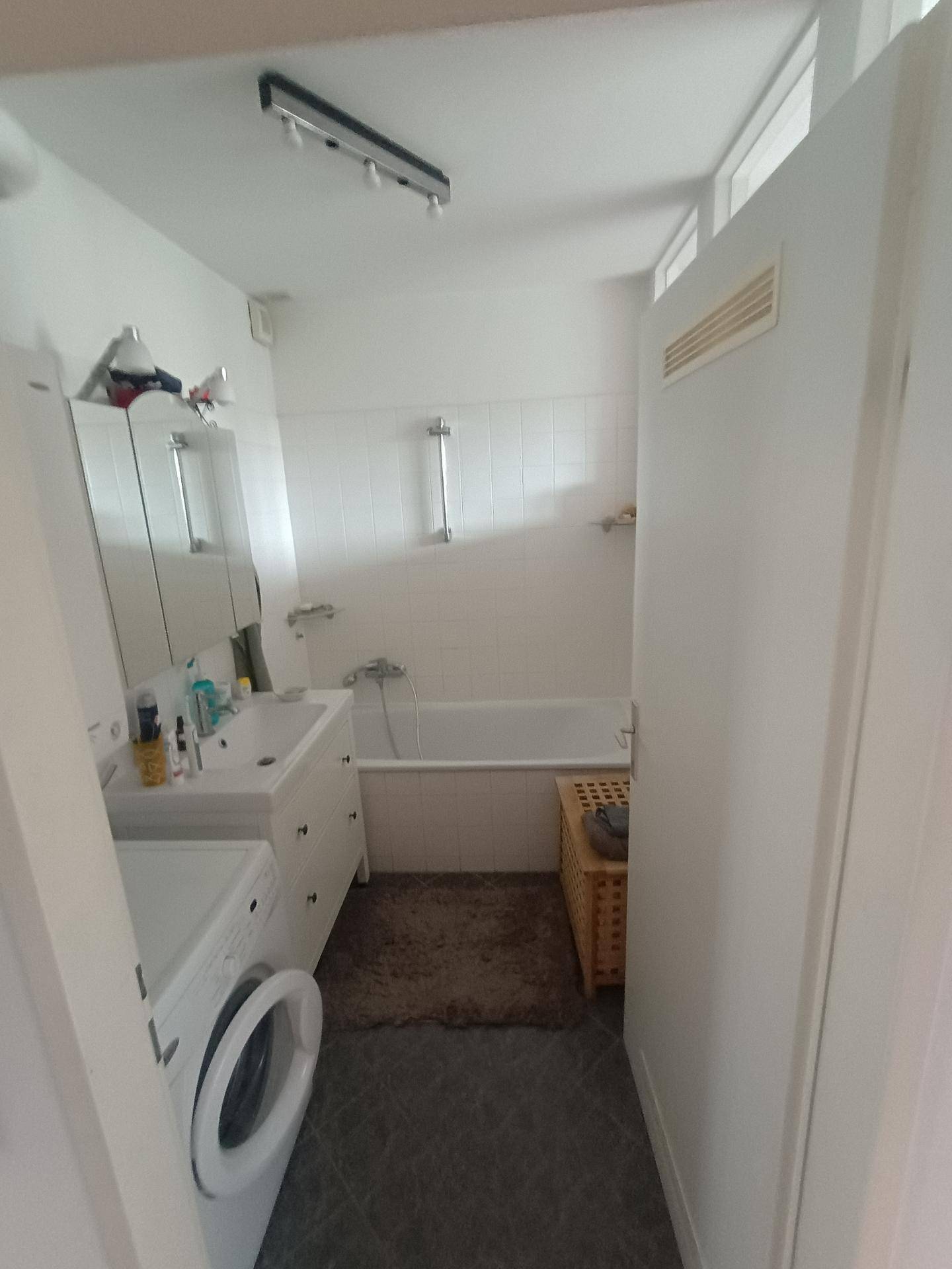 Badezimmer mit Badewanne, Waschbecken und Waschmaschine, hell gefliest.
