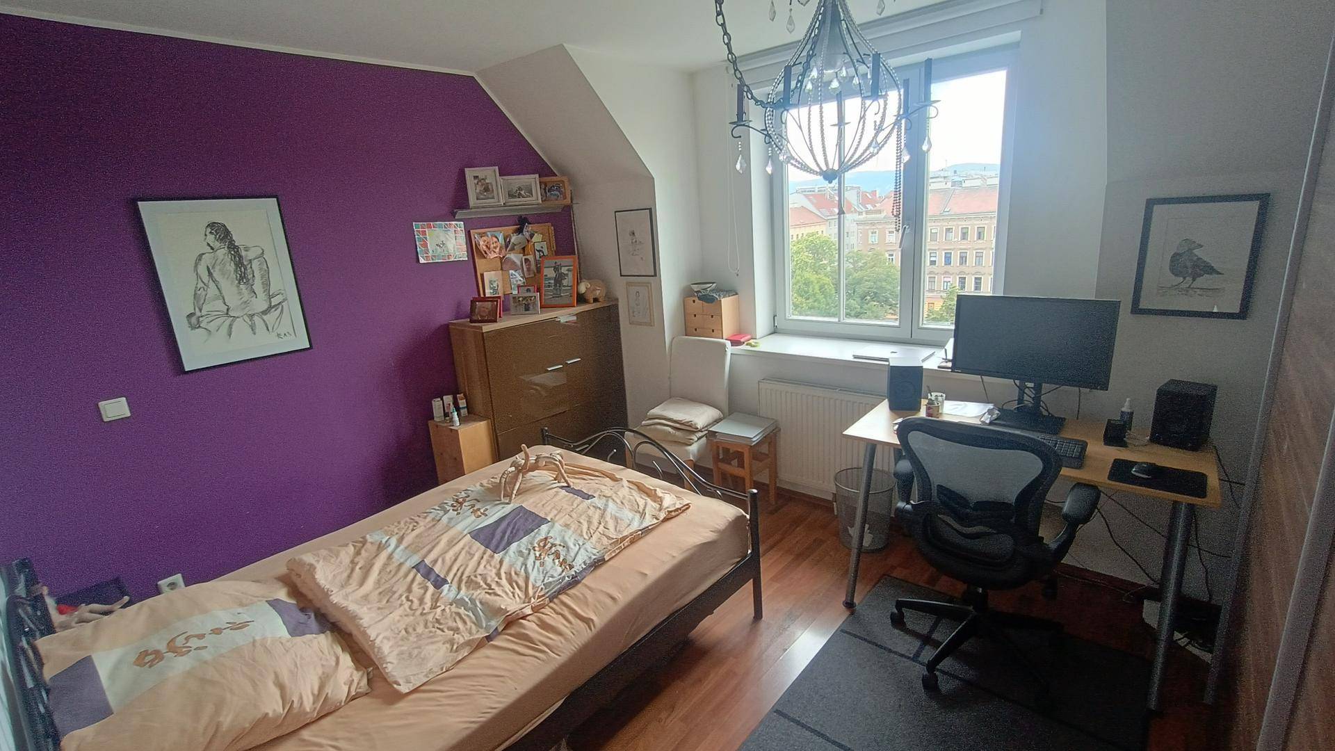 Schlafzimmer mit Bett, Schreibtisch, lila Akzentwand und Blick auf die Stadt.