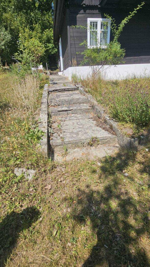 Alte Steinstufen führen durch eine grüne Wiese hinauf zum Eingang des Hauses.