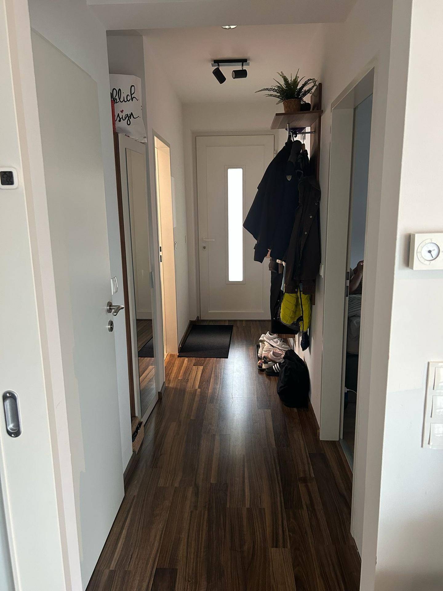 Heller Flur mit Garderobe, dunklem Laminatboden und weißer Eingangstür.
