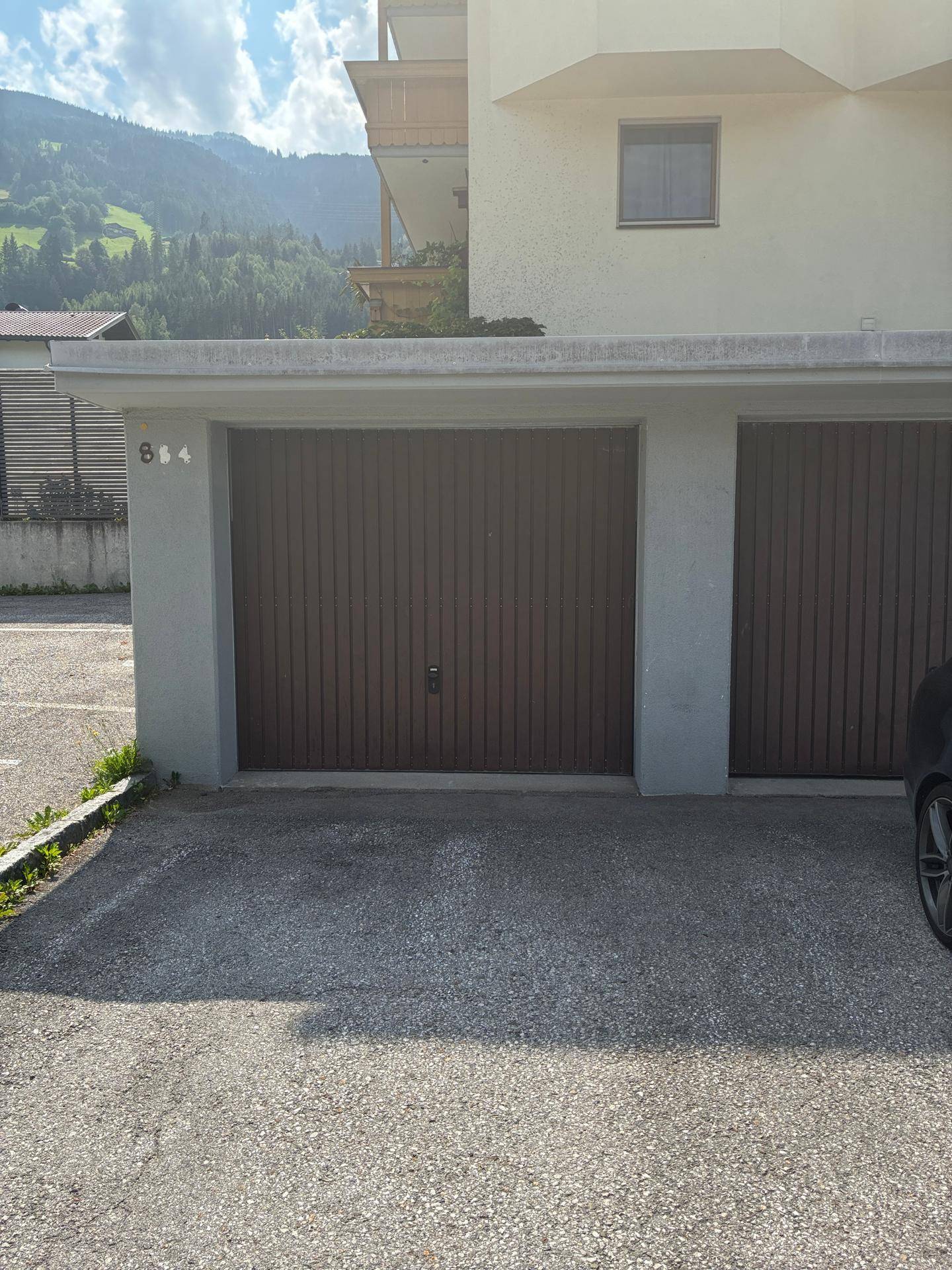 Außenansicht einer Einzelgarage mit braunem Tor und davorliegendem Stellplatz.