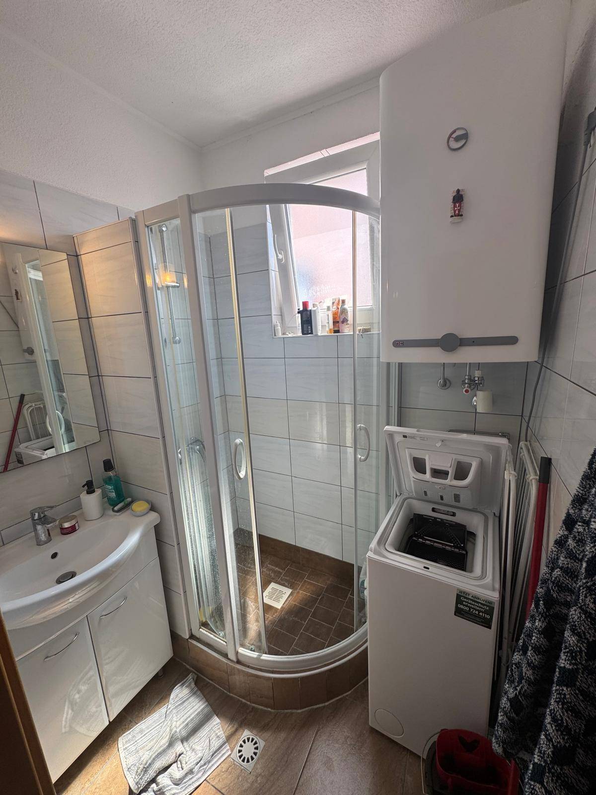 Modernes Badezimmer mit Duschkabine, Waschbecken und integrierter Waschmaschine für praktischen Komfort.