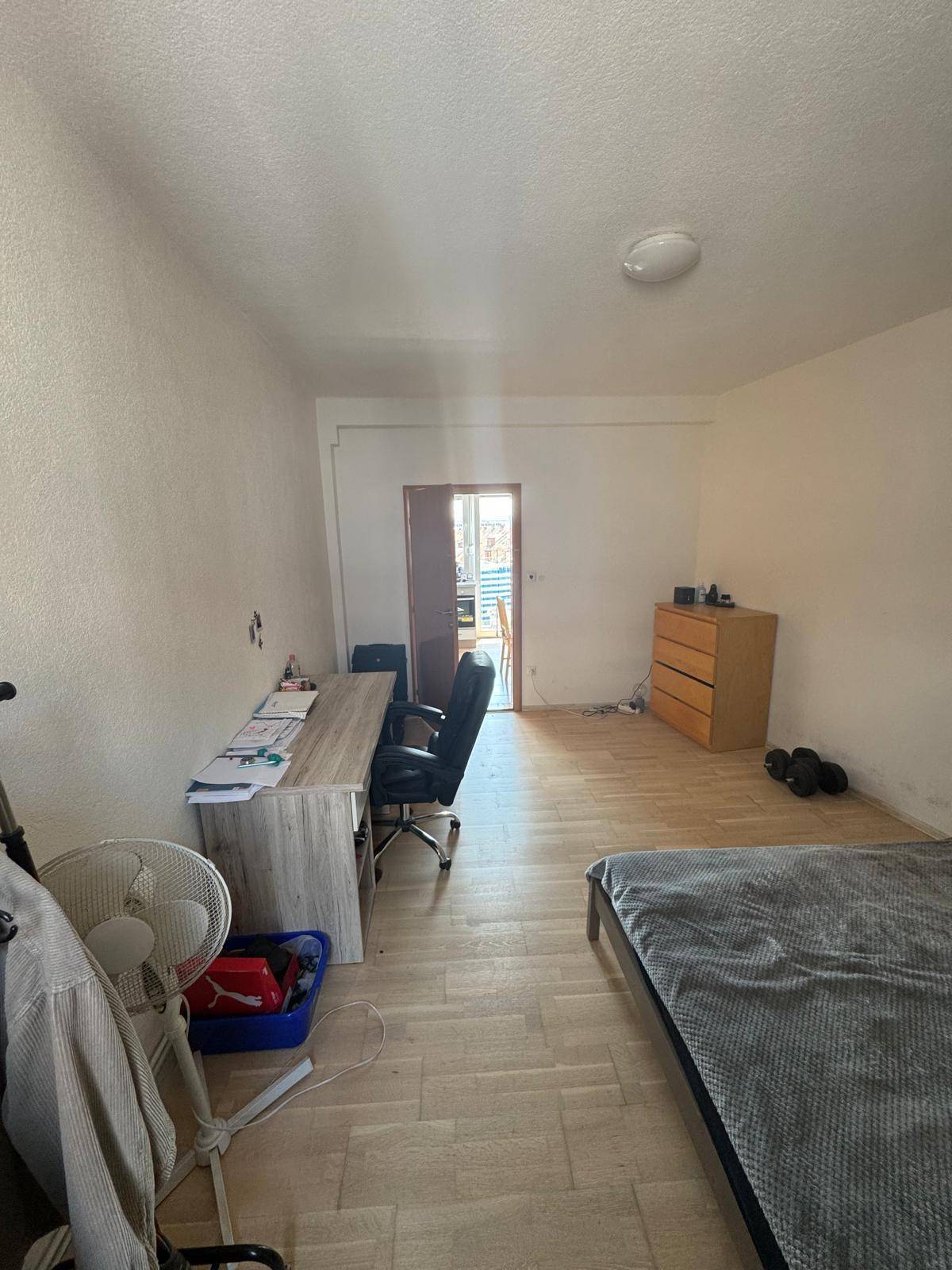 Geräumiges Schlafzimmer mit Schreibtisch, Bett und Kommode, mit Zugang zu einem weiteren hellen Raum.