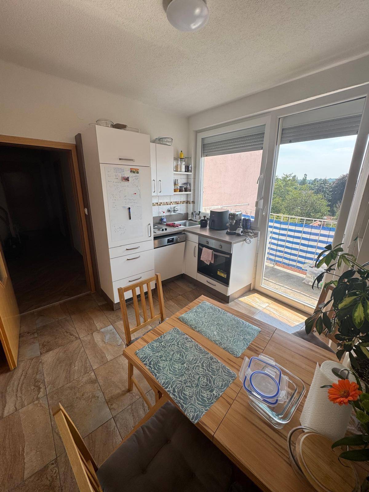Funktionale Küche mit Essbereich, weißen Schränken und direktem Zugang zu einem sonnigen Balkon.