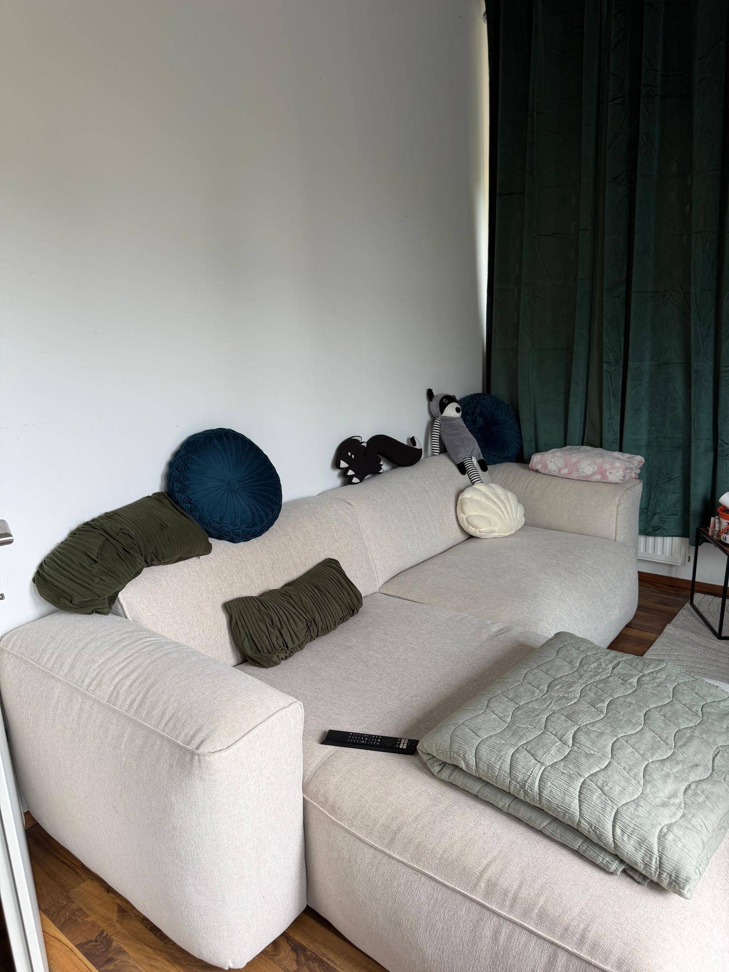 Bequemes Sofa in einem hellen Wohnzimmer mit dunklen Vorhängen und Holzboden.