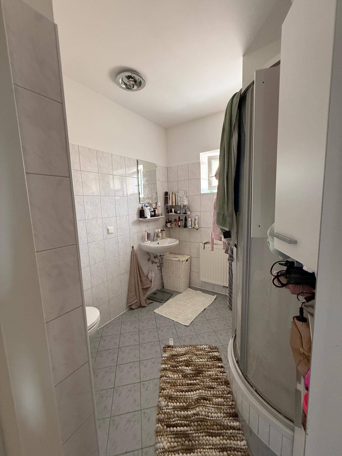 Helles Badezimmer mit Duschkabine, Waschbecken und hellen Fliesen an Wänden und Boden.