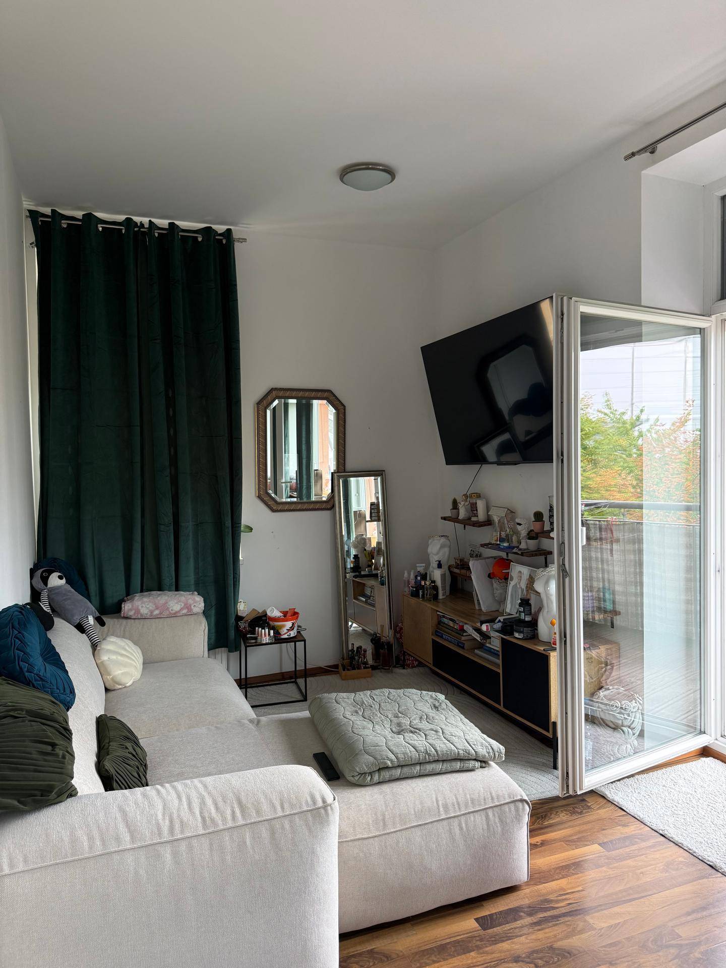 Wohnzimmer mit Sofa, Fernseher und Zugang zu einem Balkon, bietet viel Tageslicht.