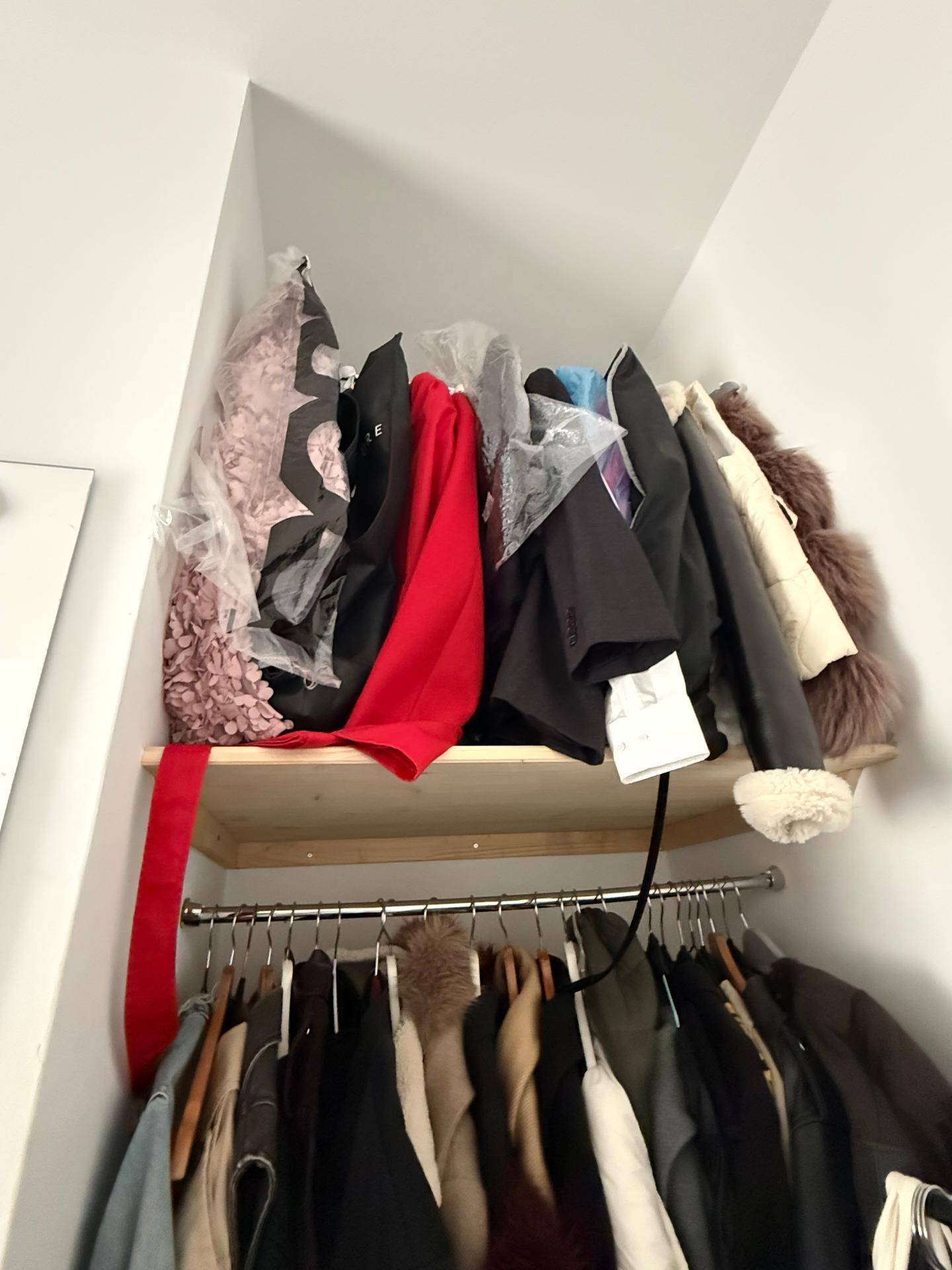 Offener Kleiderschrank mit Kleiderstange und Regal, gefüllt mit verschiedenen Kleidungsstücken.
