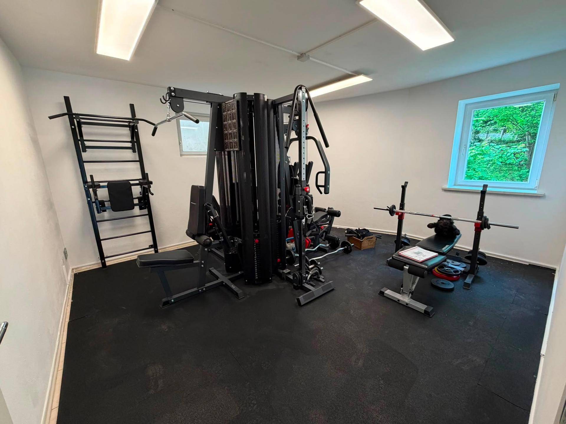 Fitnessraum im Untergeschoss mit verschiedenen Trainingsgeräten und Gummiboden.