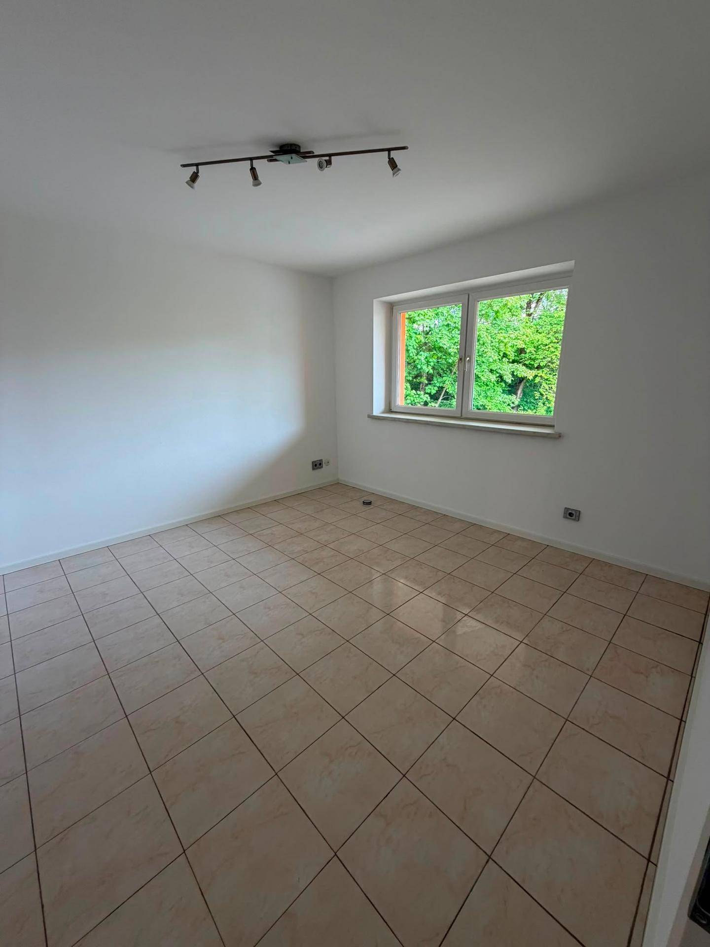 Helles Zimmer mit beigen Fliesen und Fenster mit Blick auf Bäume.