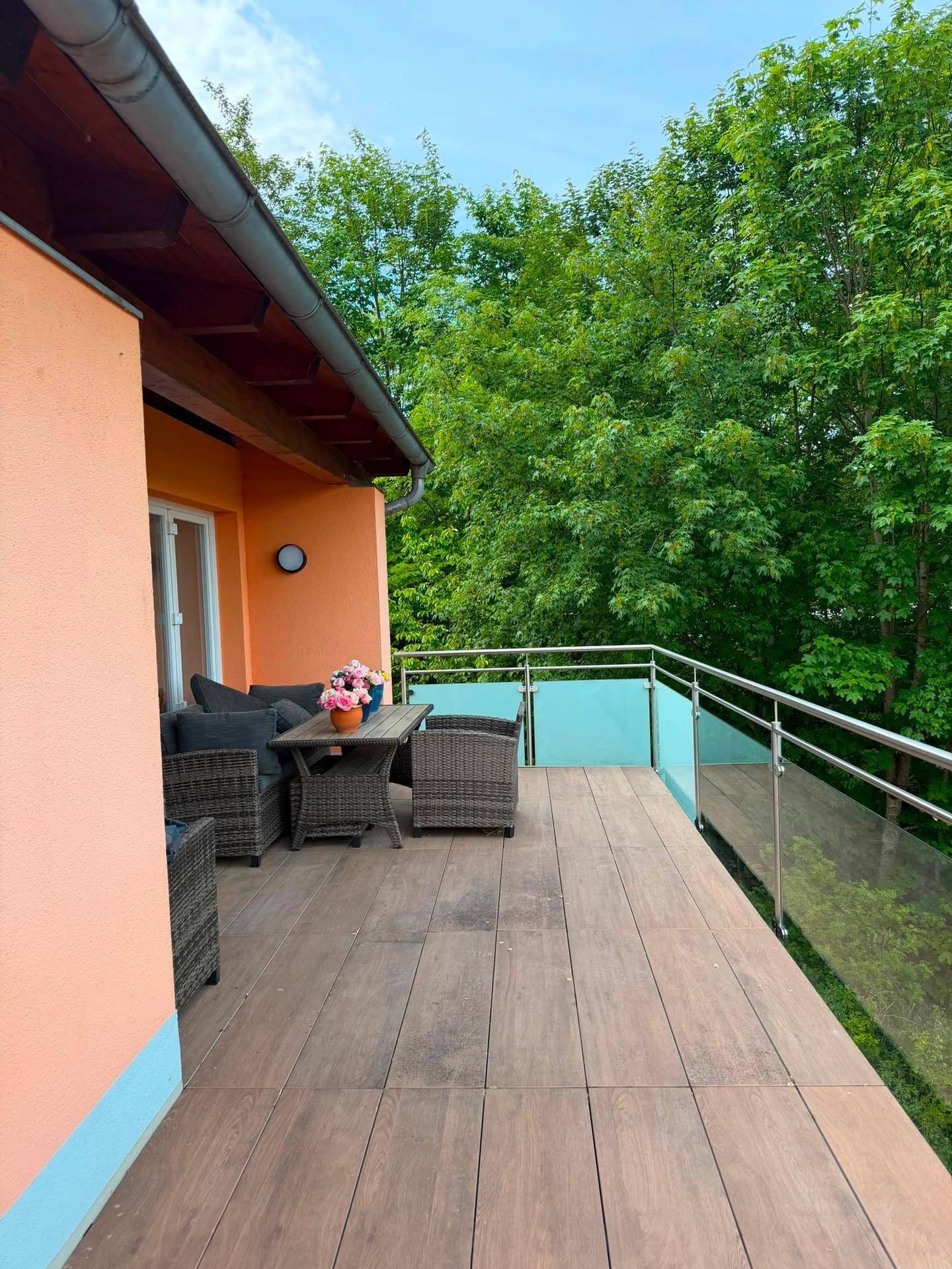 Möblierter Balkon mit Holzboden und Blick auf grüne Bäume.