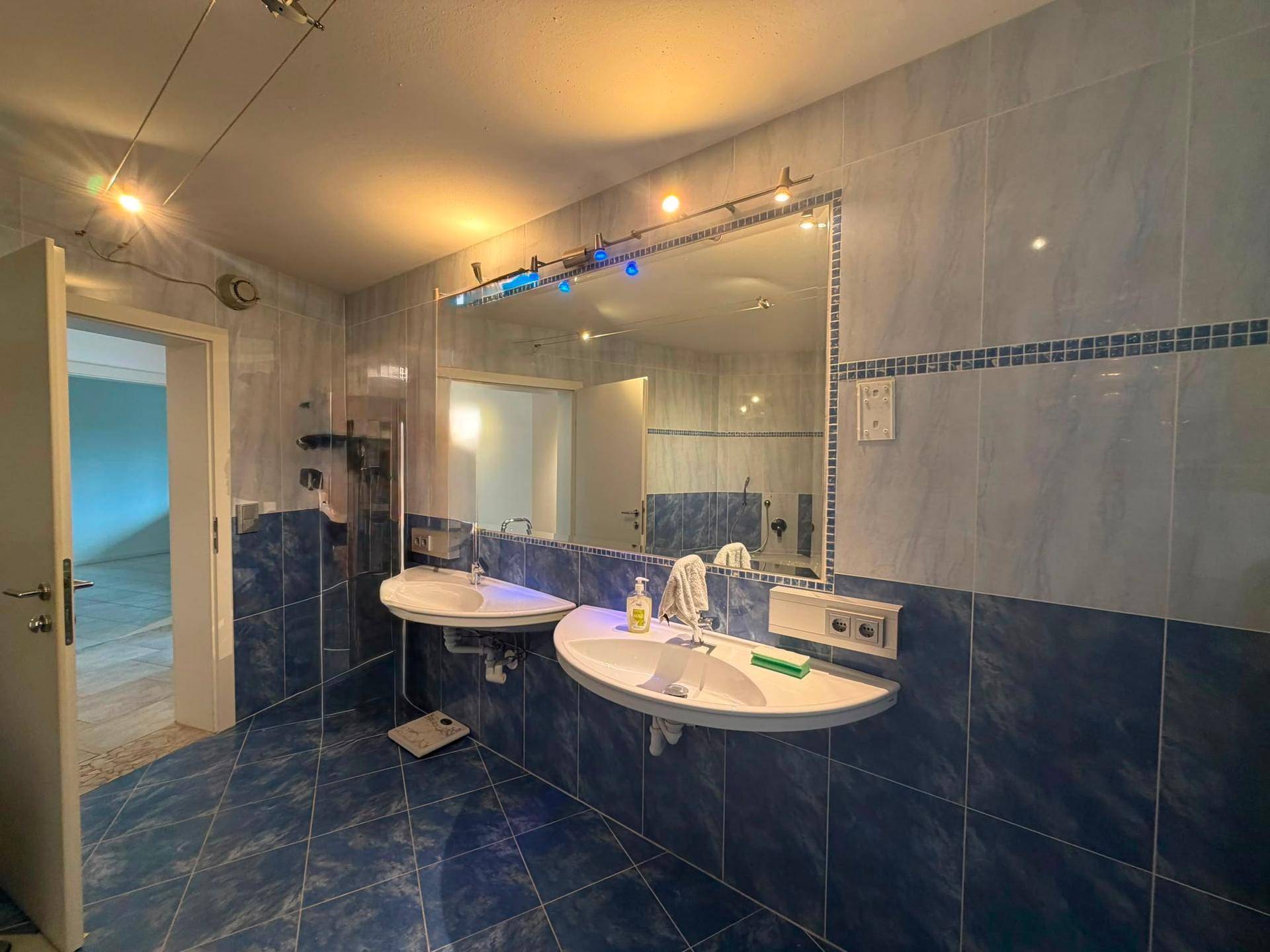 Badezimmer mit Doppelwaschbecken, großem Spiegel und blauen Fliesen.