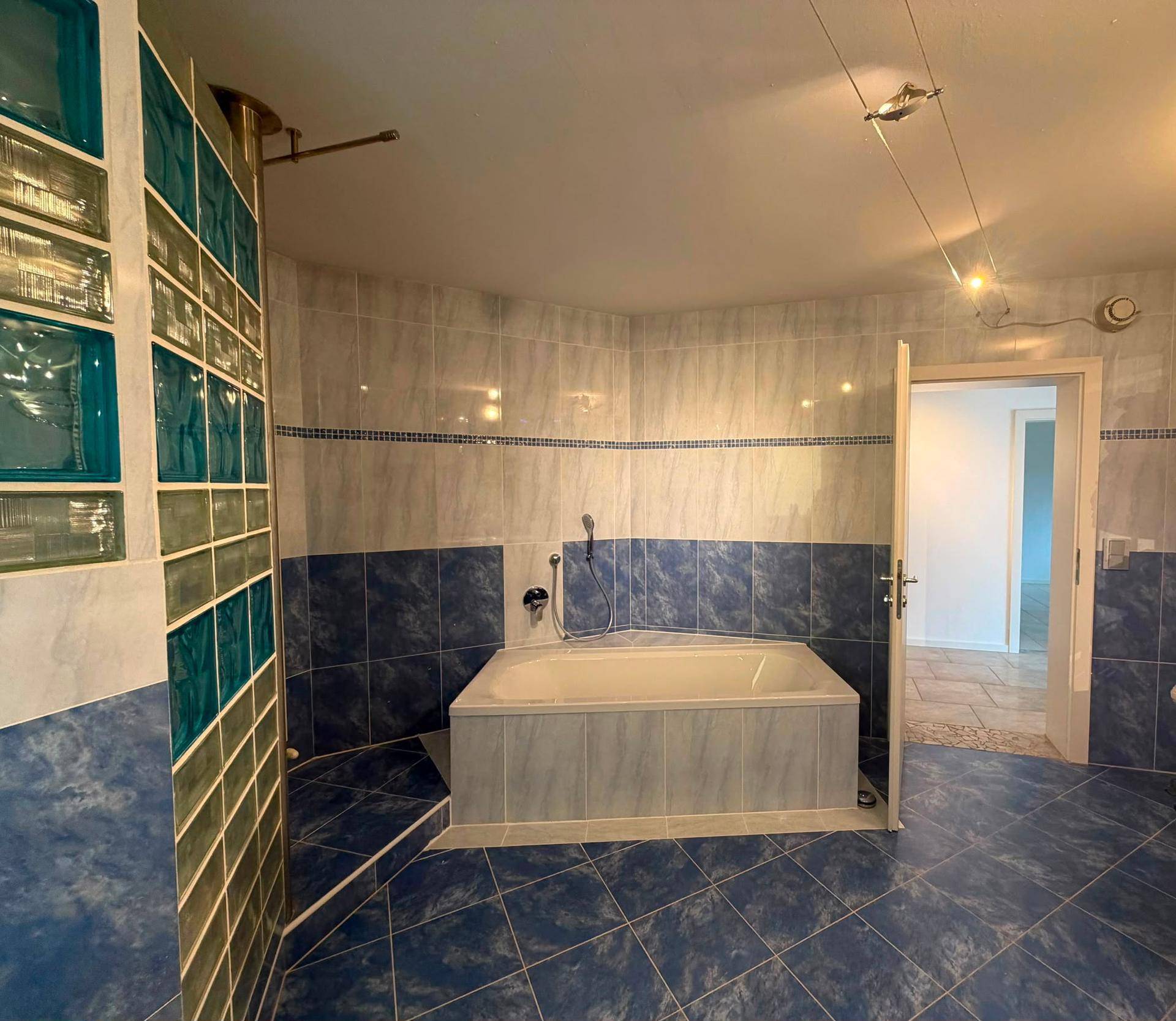 Badezimmer mit blauen Fliesen, Glasbausteinen und einer eingebauten Badewanne.