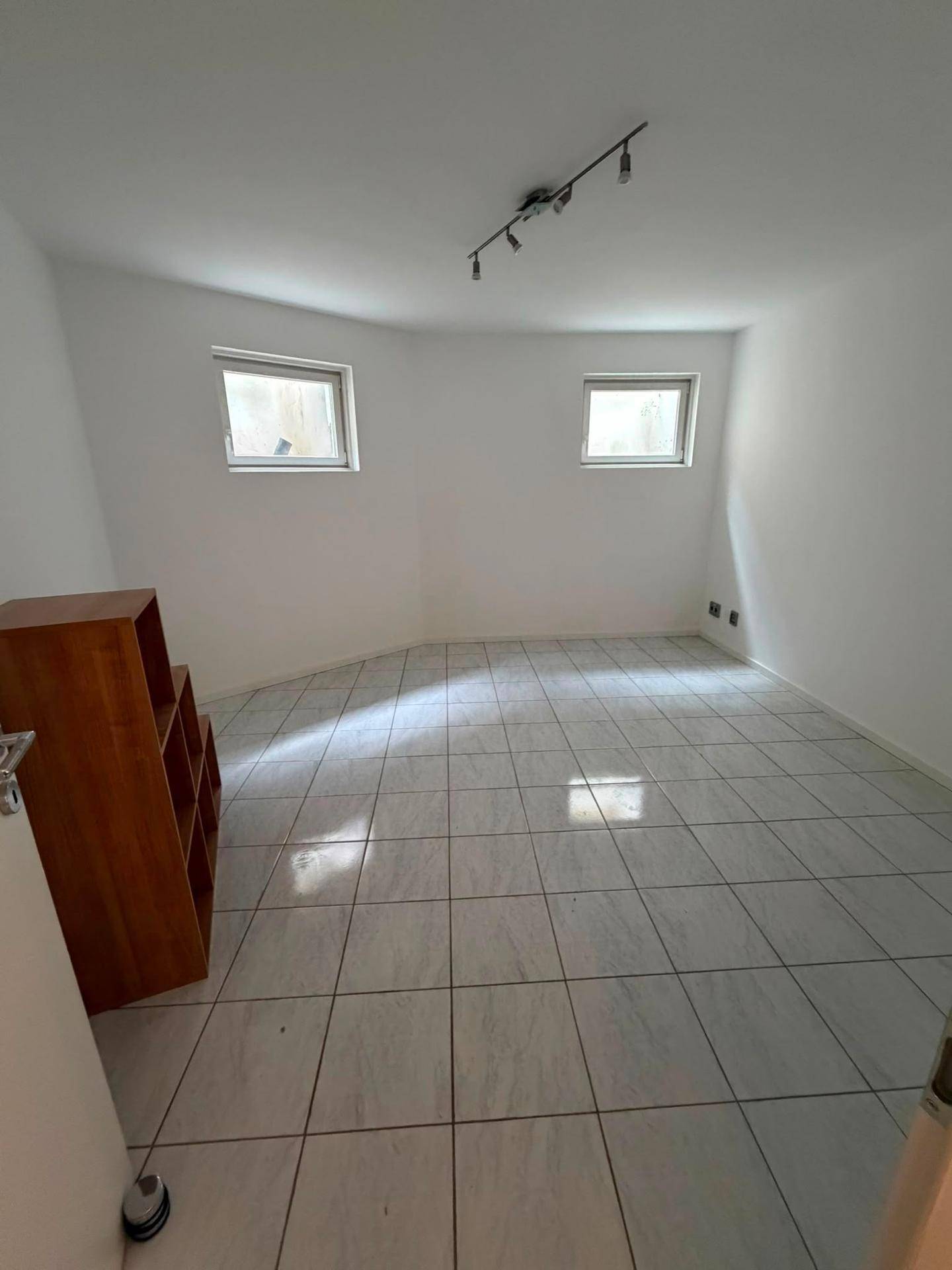 Kleiner Raum mit Fliesenboden und zwei Fenstern, ideal als Büro oder Gästezimmer.