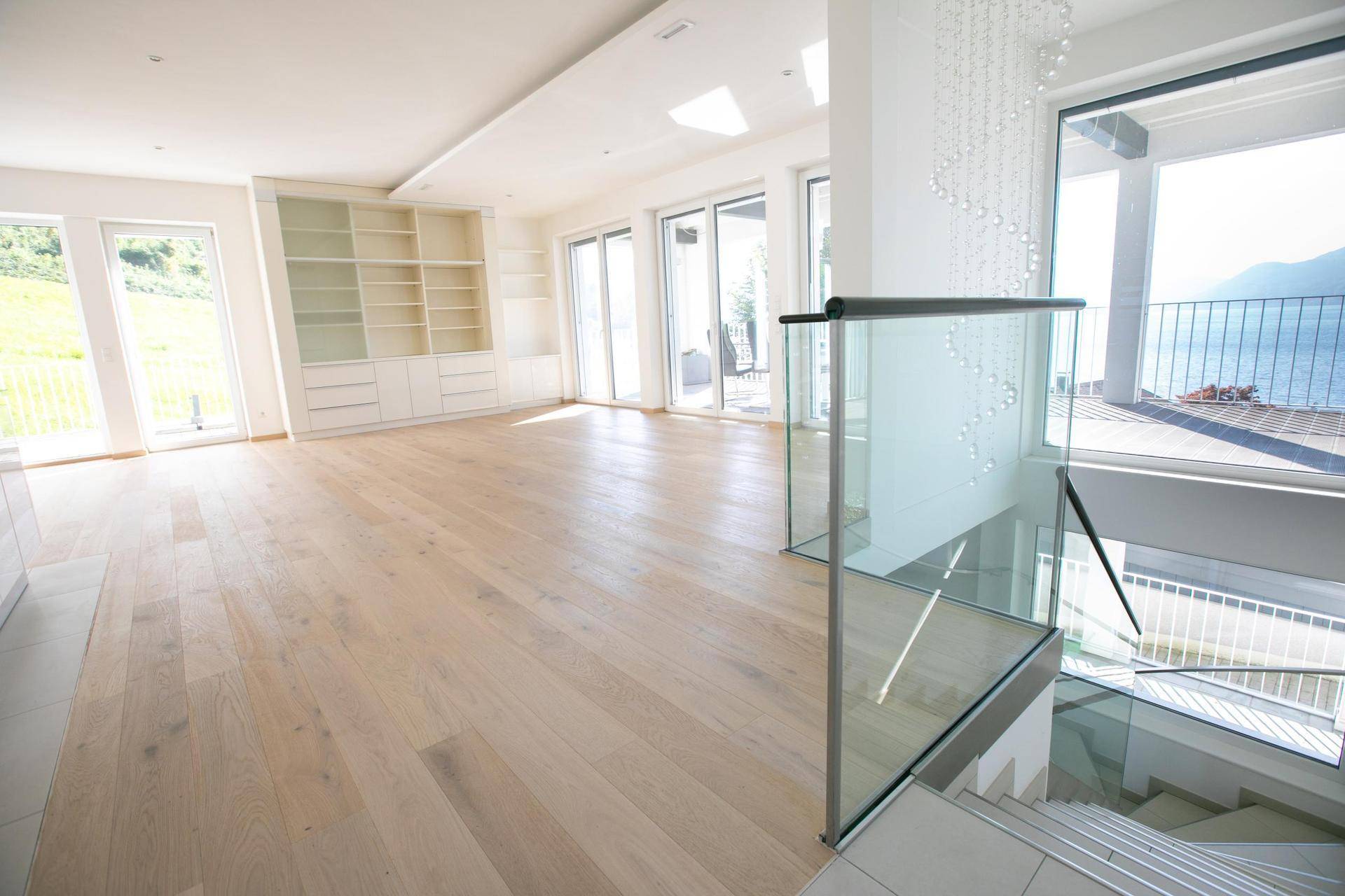 Heller Wohnbereich mit Holzboden, Einbauregalen und großen Fenstern, die einen weiten Seeblick ermöglichen.