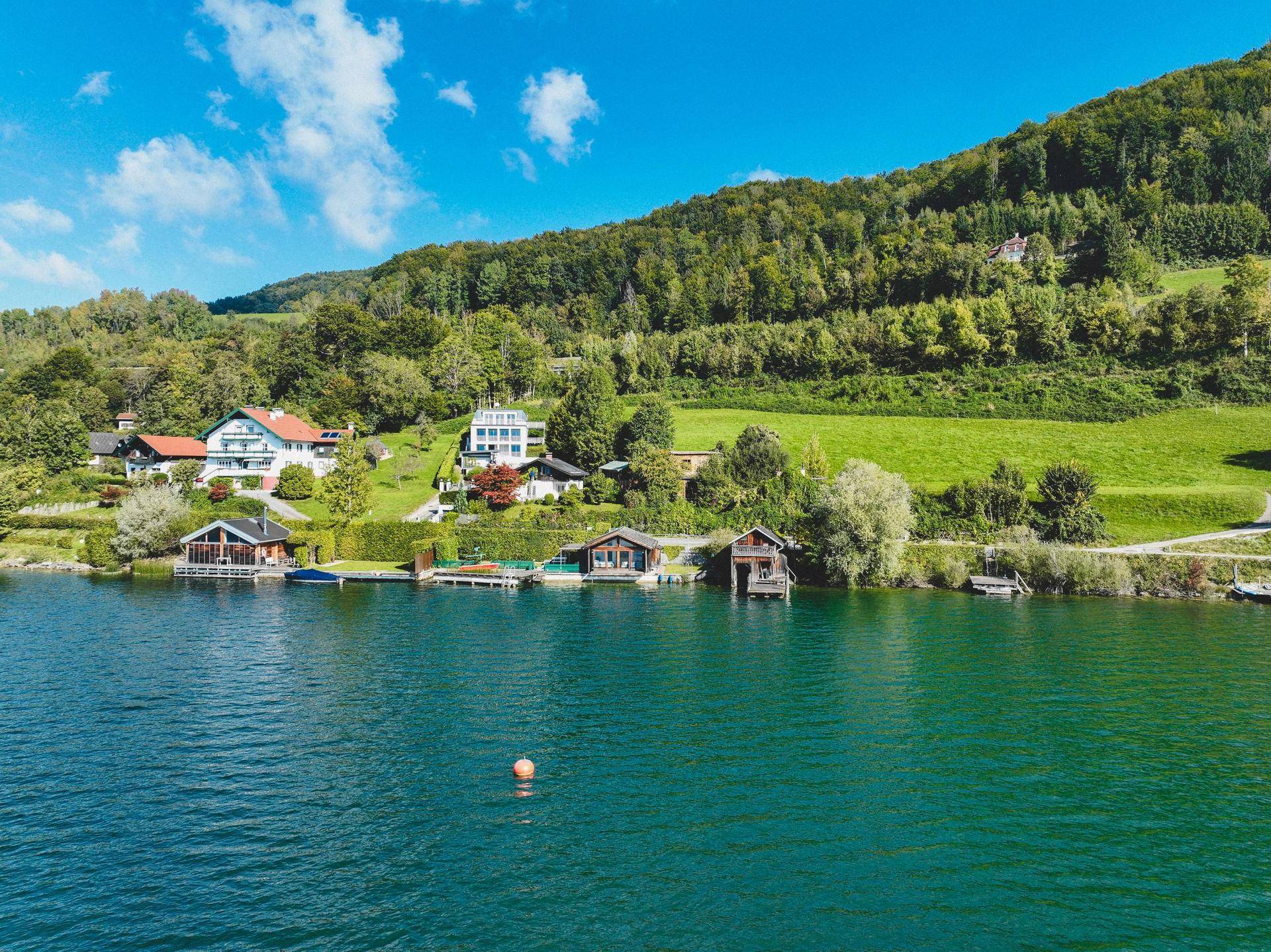 Panoramablick auf die Häuser am Seeufer, umgeben von Bergen und üppiger grüner Natur.