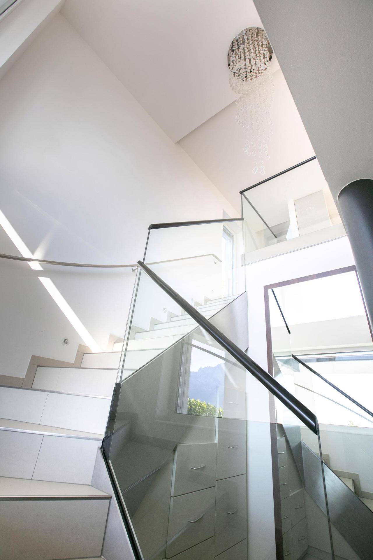 Elegante Treppe mit Glasgeländer und einem modernen Kronleuchter, die die Etagen verbindet.