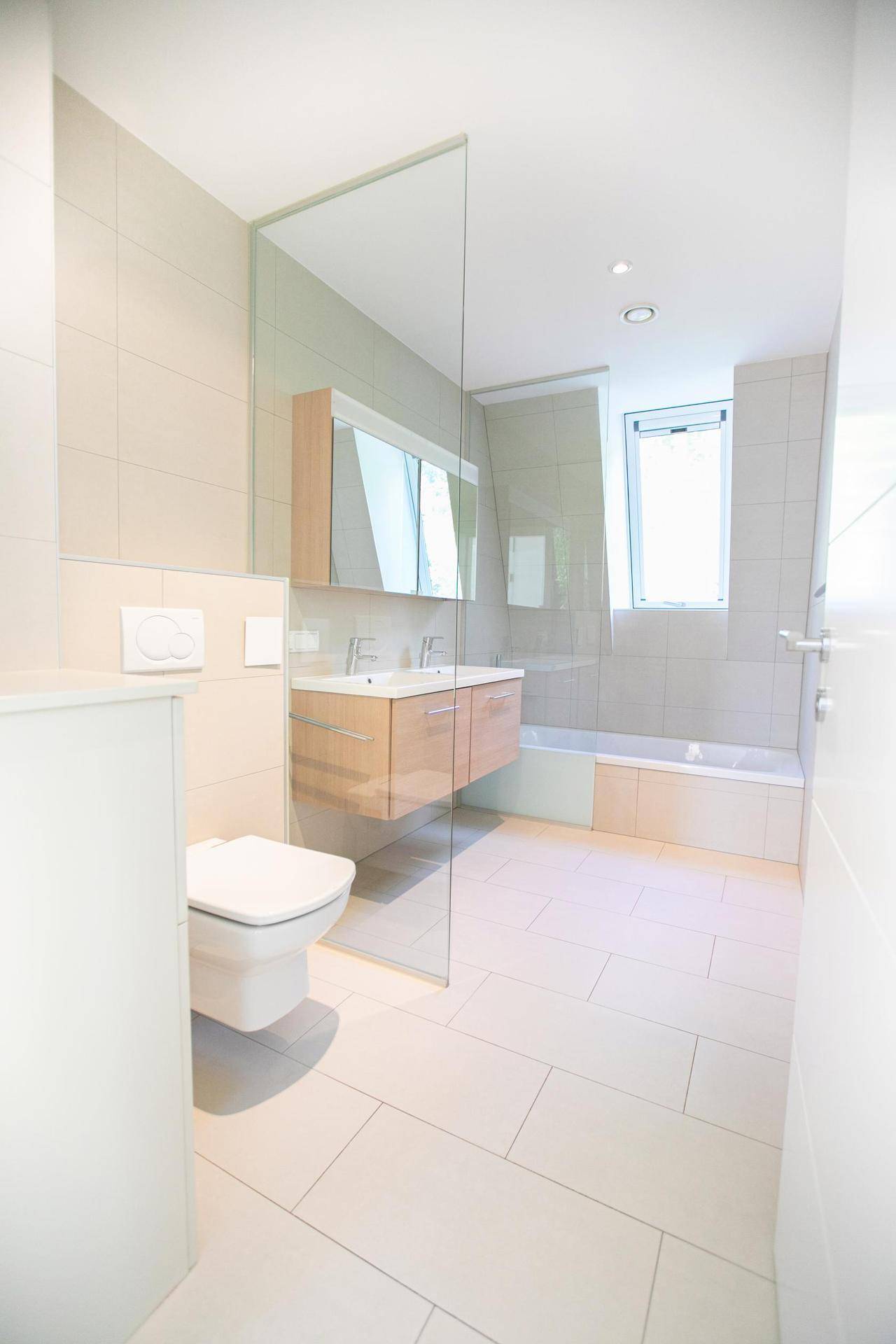 Modernes Badezimmer mit WC, Doppelwaschbecken, Badewanne und Duschbereich, hell gefliest.